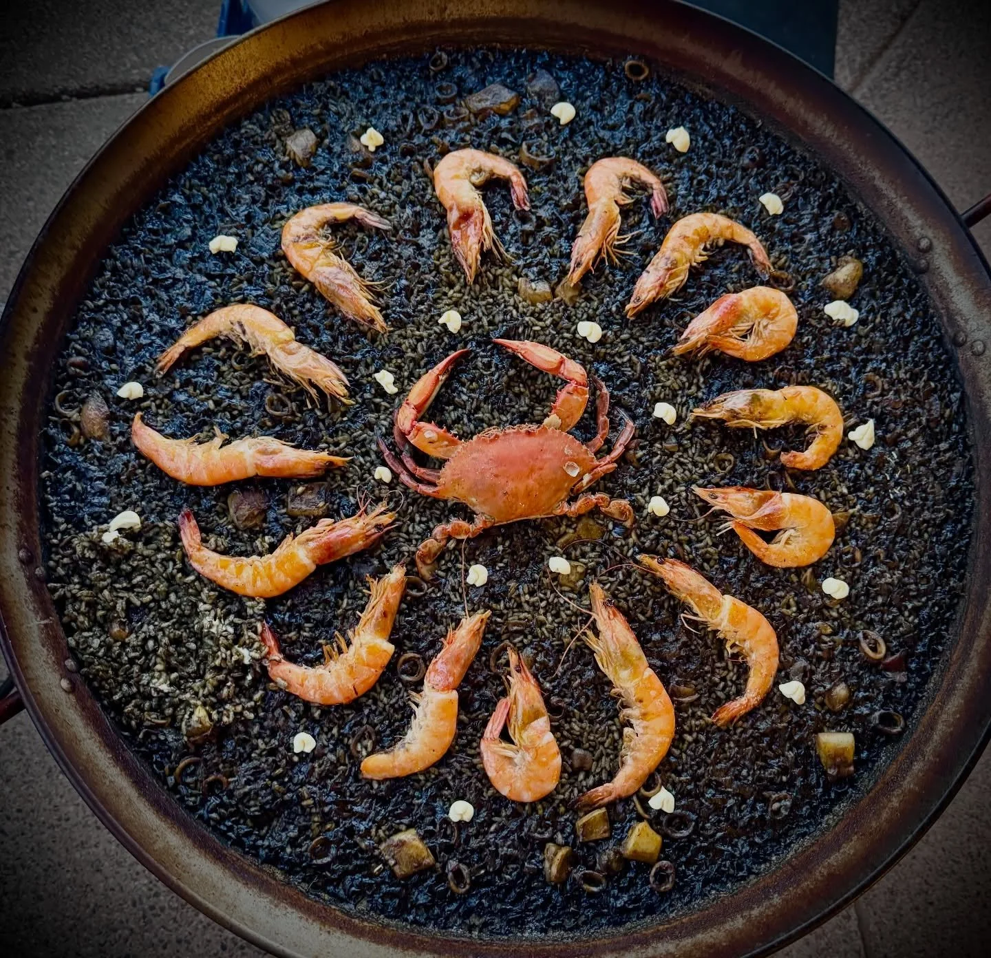 Black Paella, or Arr&ograve;s Negre, serves as a striking centerpiece that elevates any event from a simple meal to a sophisticated sensory experience. The deep, obsidian hue of the squid-ink rice provides a dramatic backdrop for vibrant seafood and 