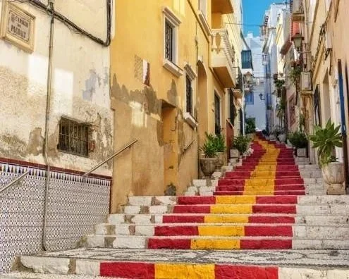 Colorful painted stairs in a narrow European city alleyway with plants on sides.