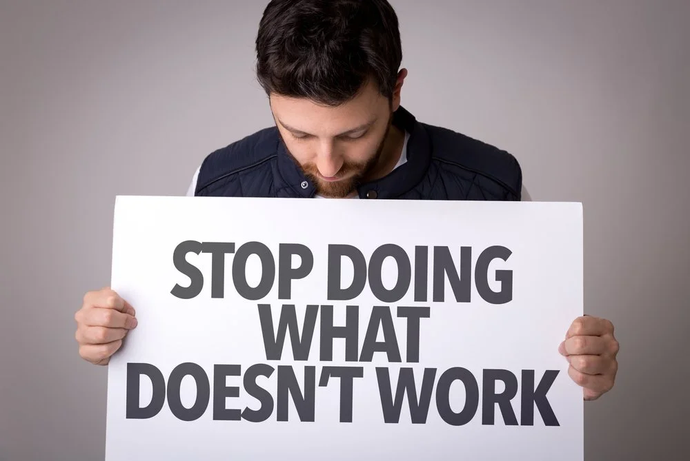 Man holding a sign that says 'STOP DOING WHAT DOESN'T WORK'.