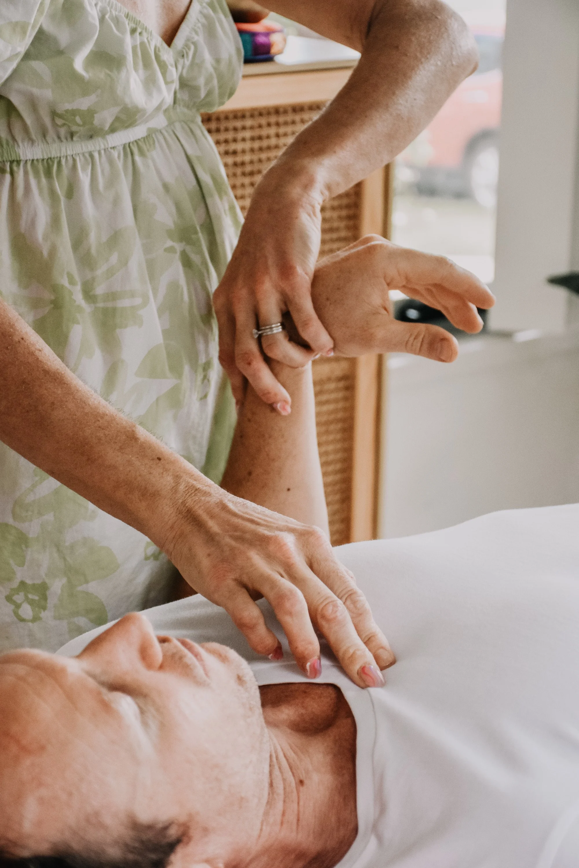 A person receiving a massage, with their head resting on a white surface, while a therapist applies pressure to their shoulder and arm.