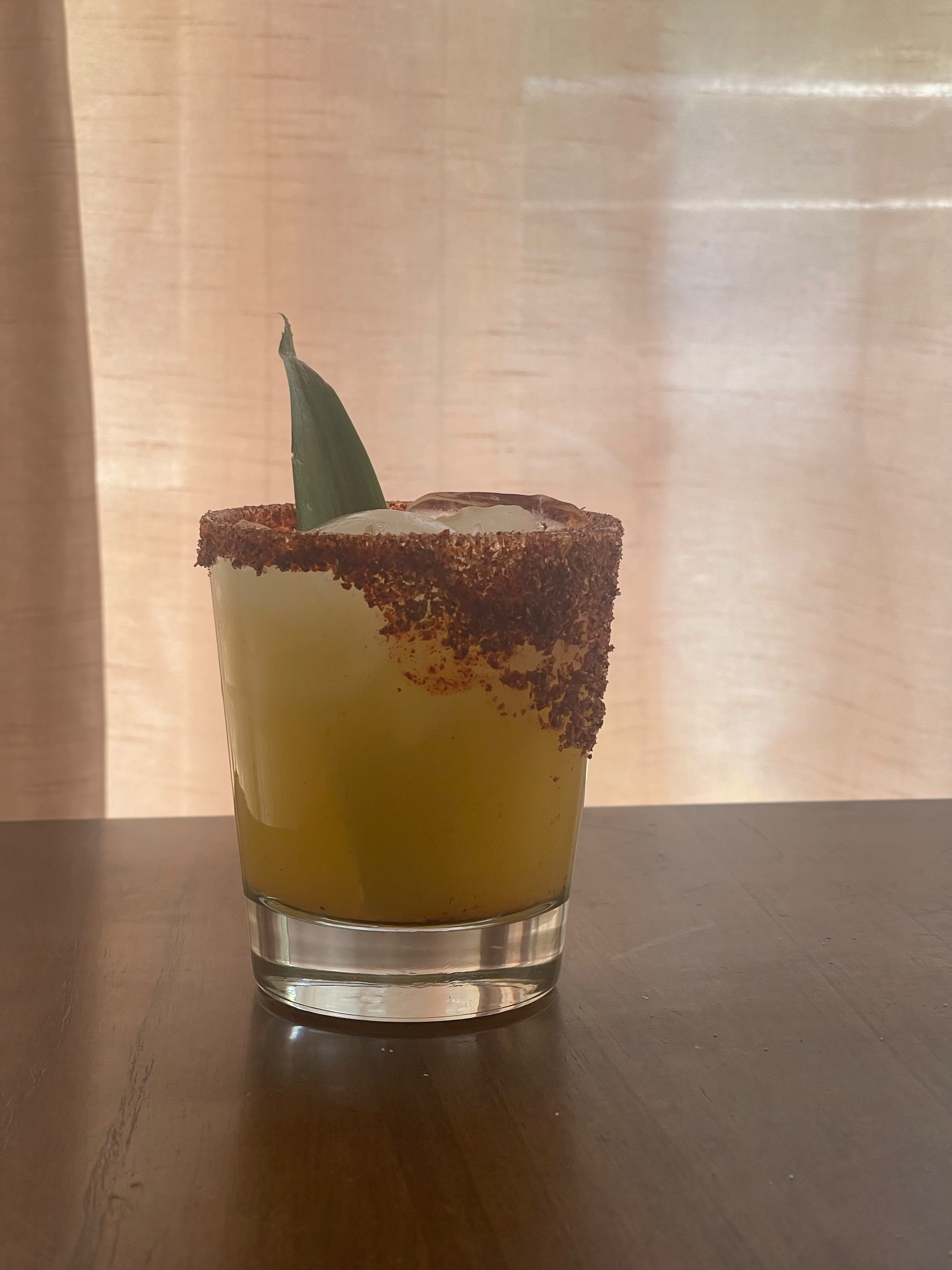Cocktail in a glass with a salted rim, garnished with a green leaf, on a wooden surface.
