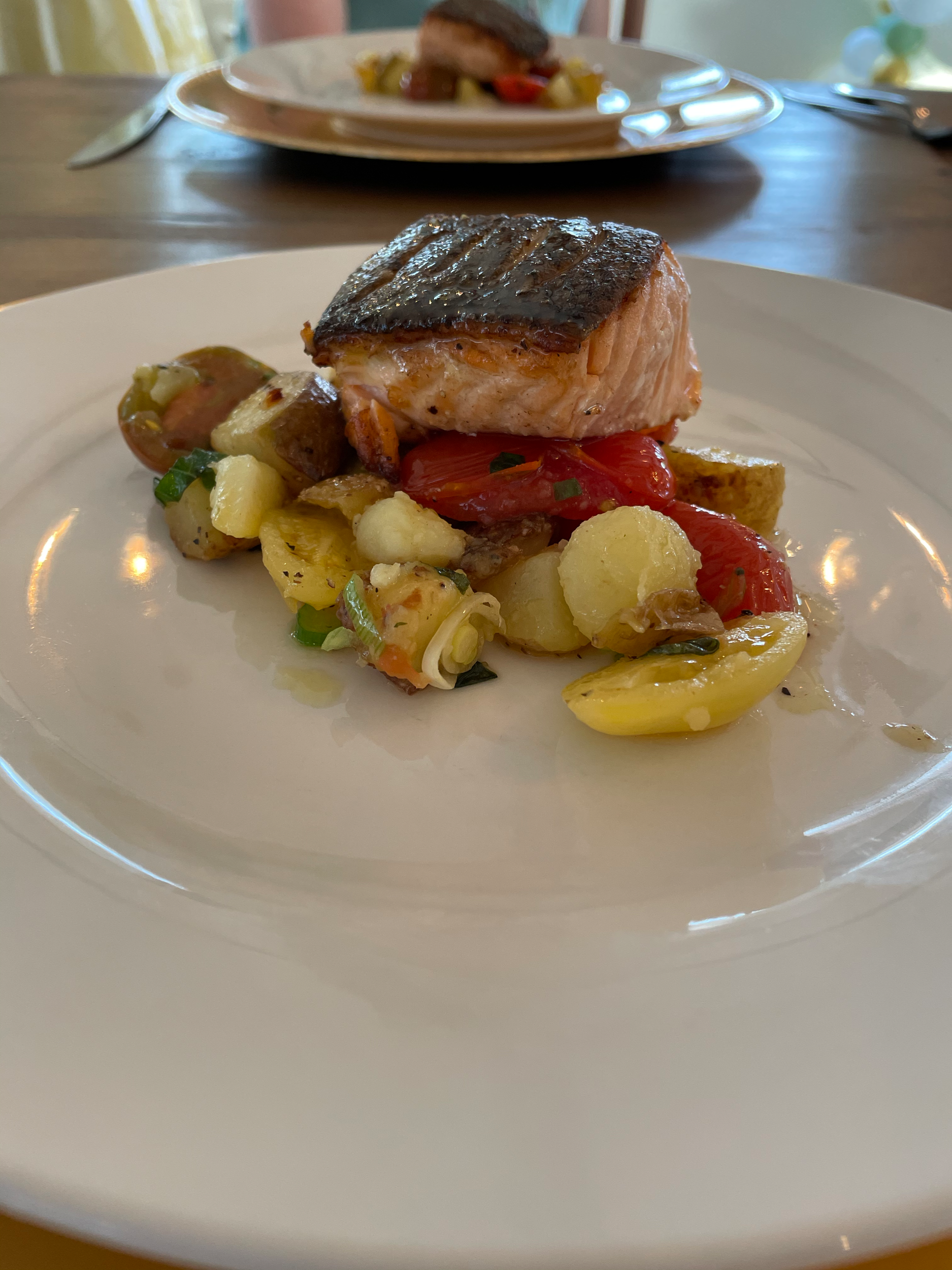 A plate with a piece of cooked salmon, roasted vegetables including red and yellow peppers, cauliflower, and potatoes.