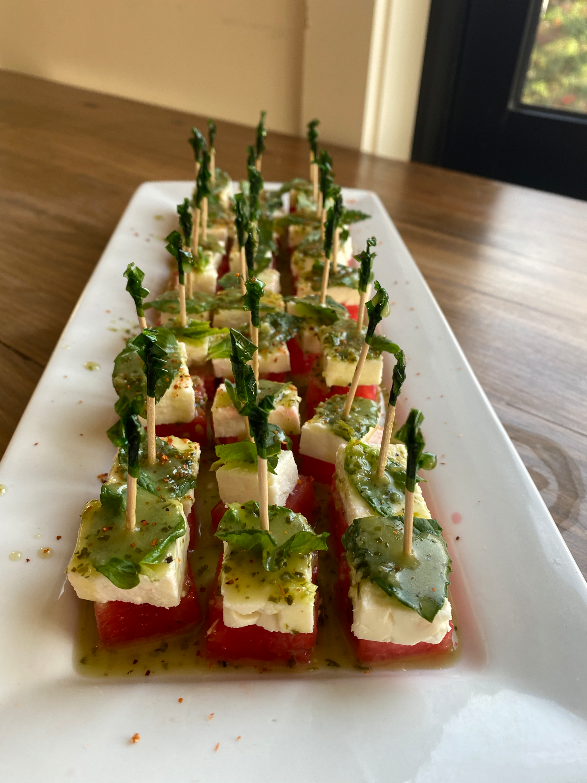 Caprese salad skewers with mozzarella, tomato, basil, and balsamic glaze on a white plate.