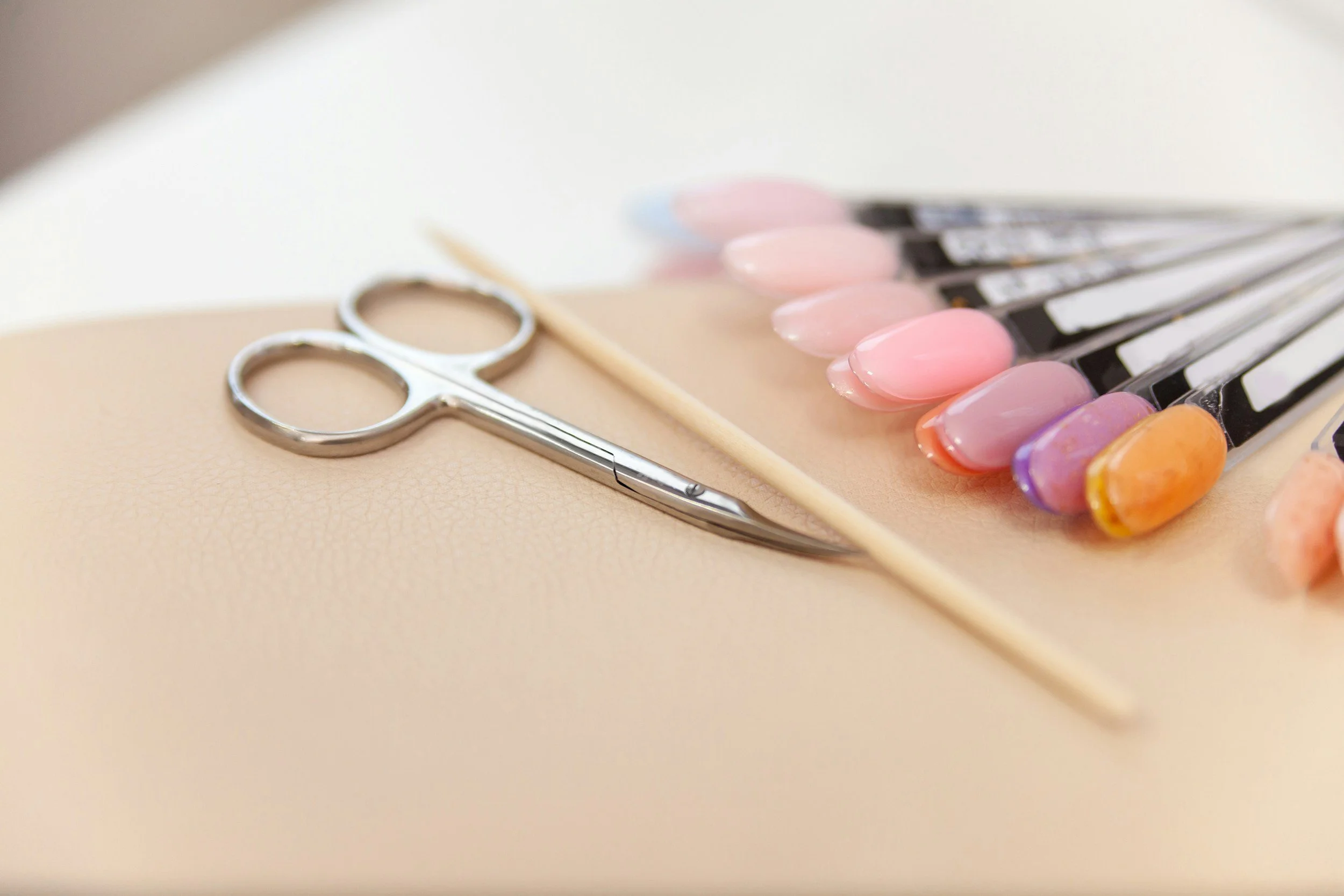 Nail polish color palette, manicure scissors, and a wooden cuticle stick on a beige surface.