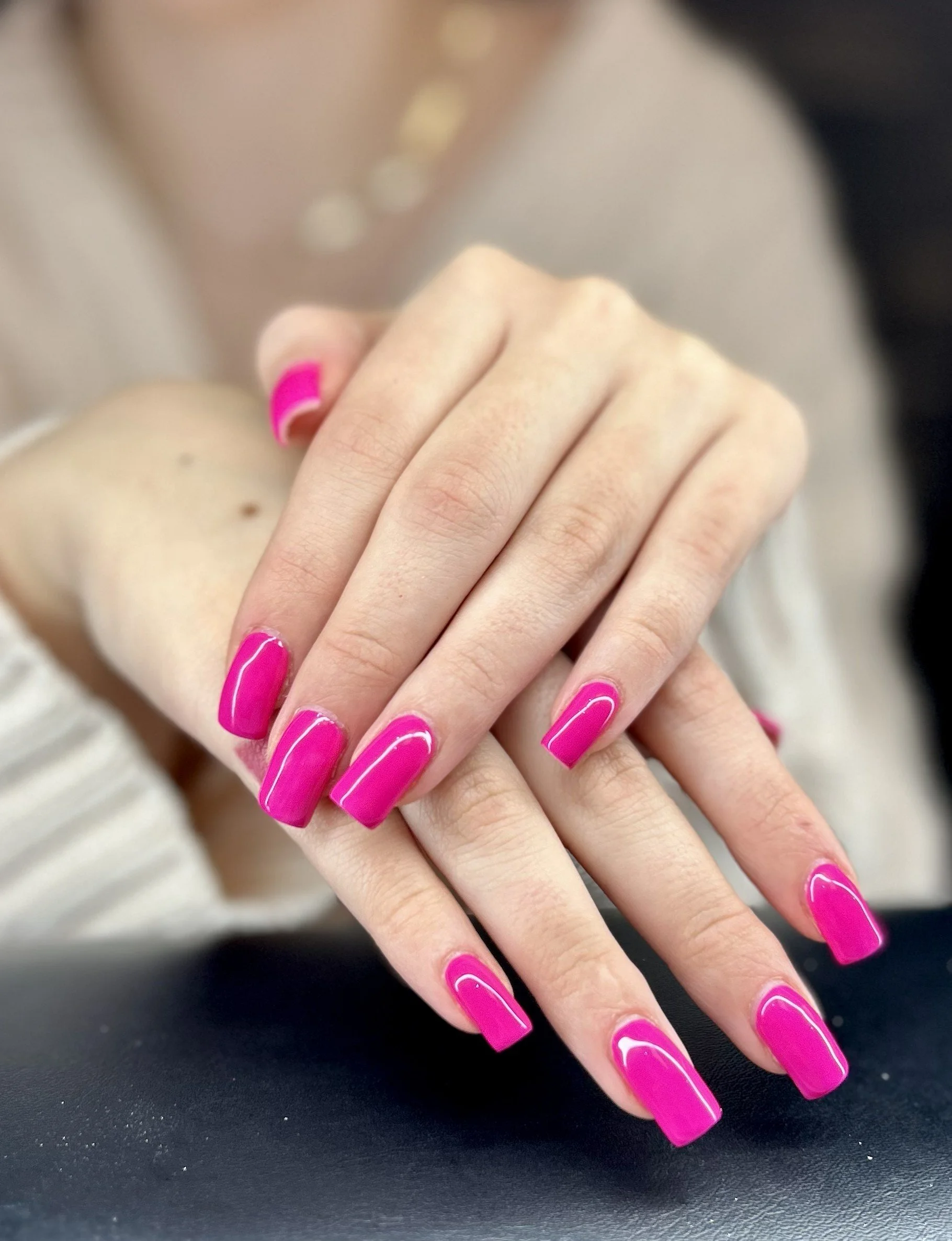 Close-up of a person's hands with bright pink, glossy, square-shaped manicured nails.