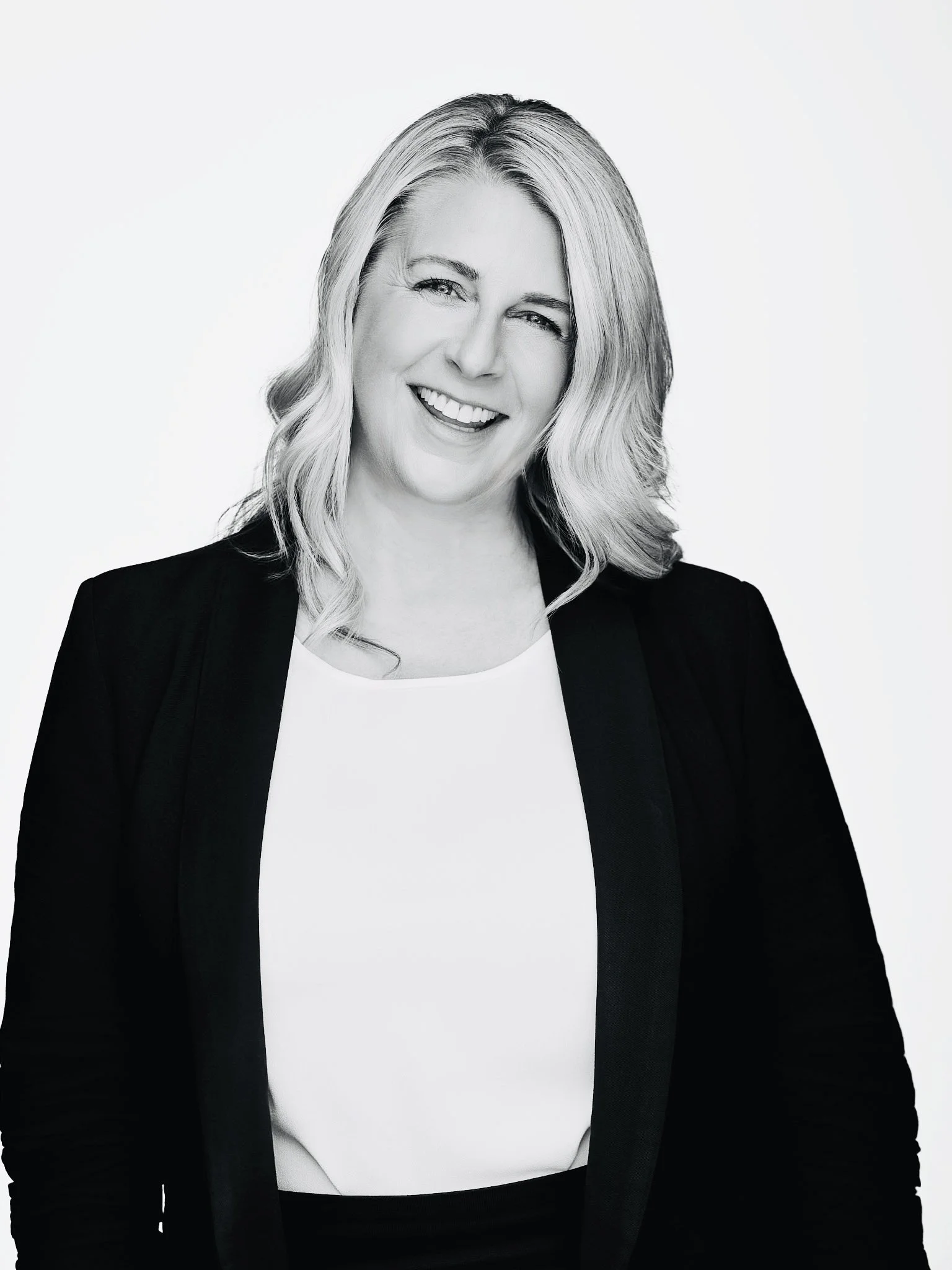 Black and white portrait of a smiling woman with shoulder-length wavy hair, wearing a blazer over a white top.