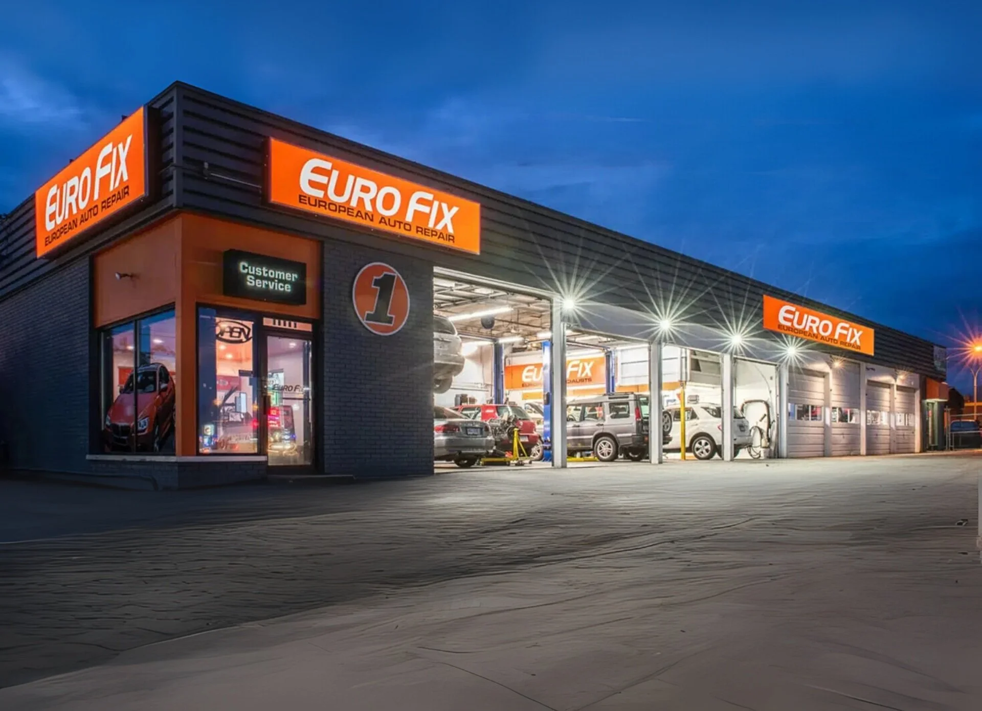 Exterior of a Euro Fix auto repair shop during evening with multiple cars inside, signage for customer service, and bright lighting.