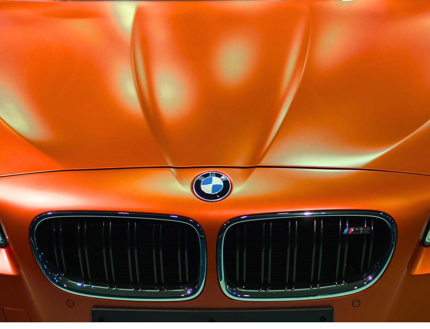 Front view of a metallic orange BMW car with the BMW logo on the hood and kidney grill design.