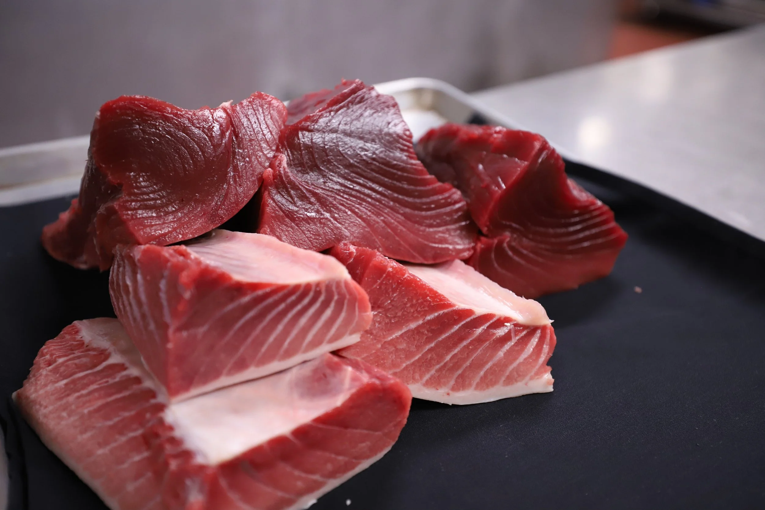 Slices of fresh tuna belly on a black cutting board.