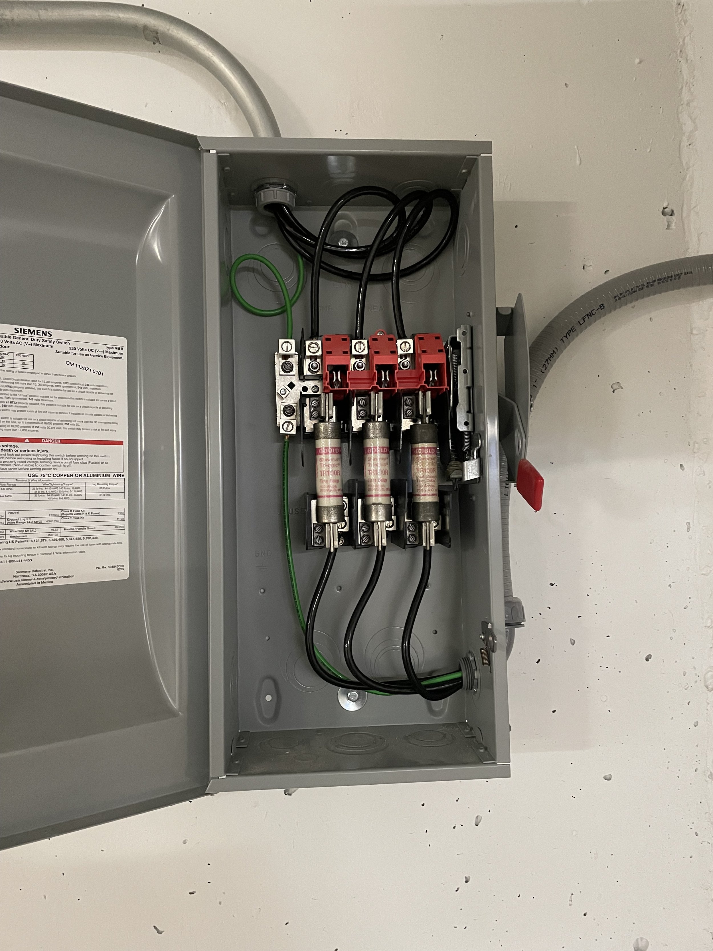 Open electrical box with three fuses, black wires, and green grounding wire inside.