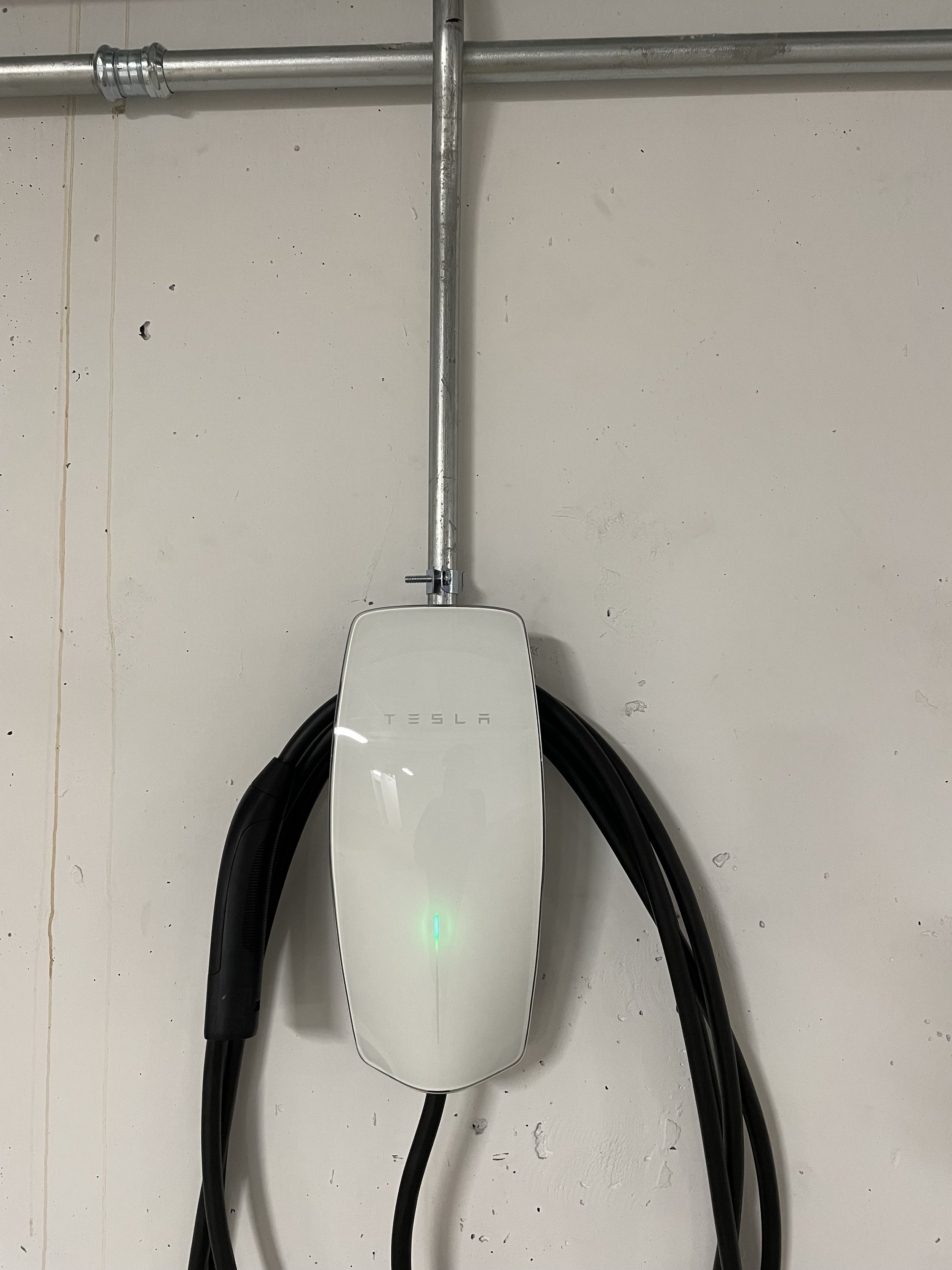 Tesla electric vehicle wall charger mounted on a white wall with black charging cables connected.
