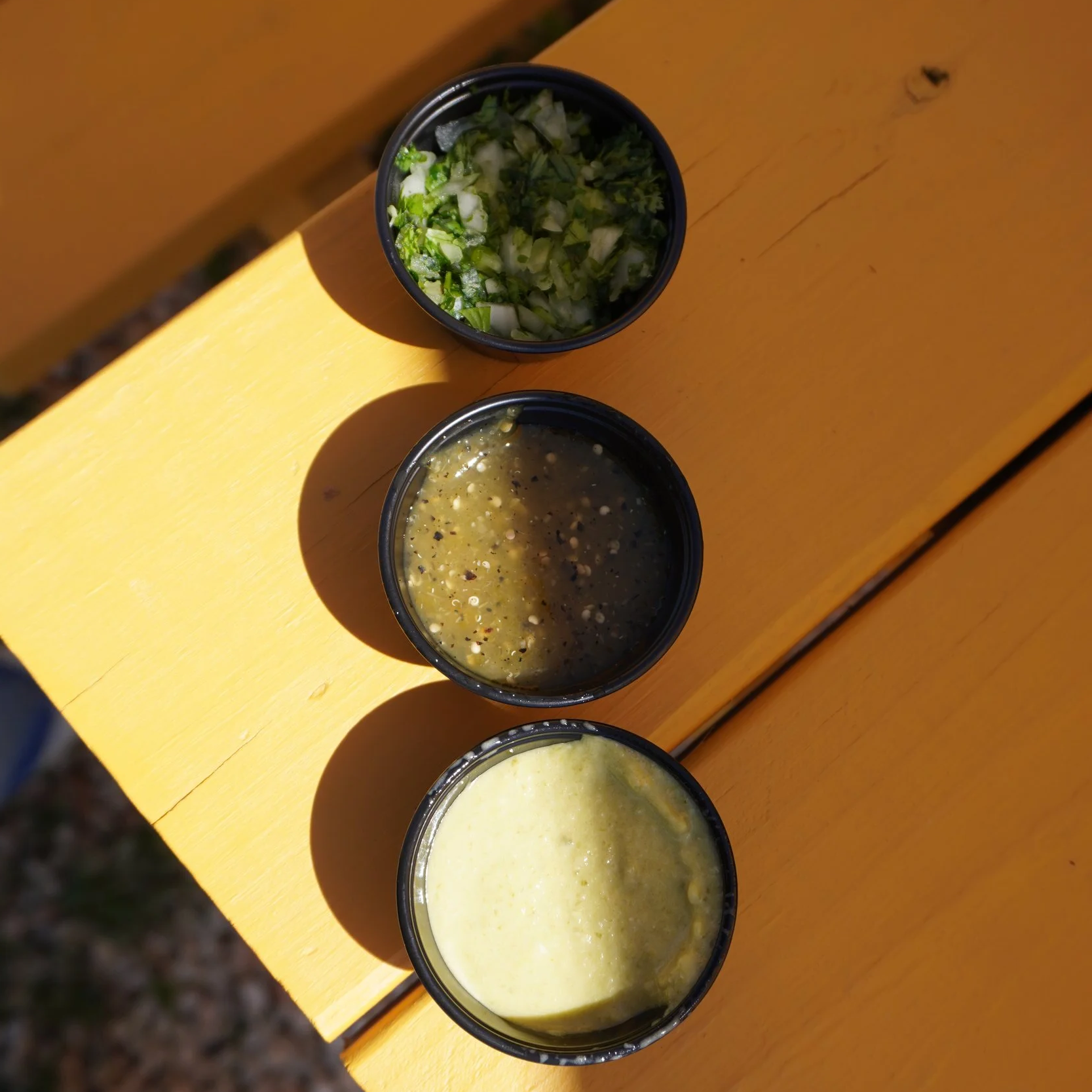 three black plastic cups filled with green salsas and garnish onion/cilantro