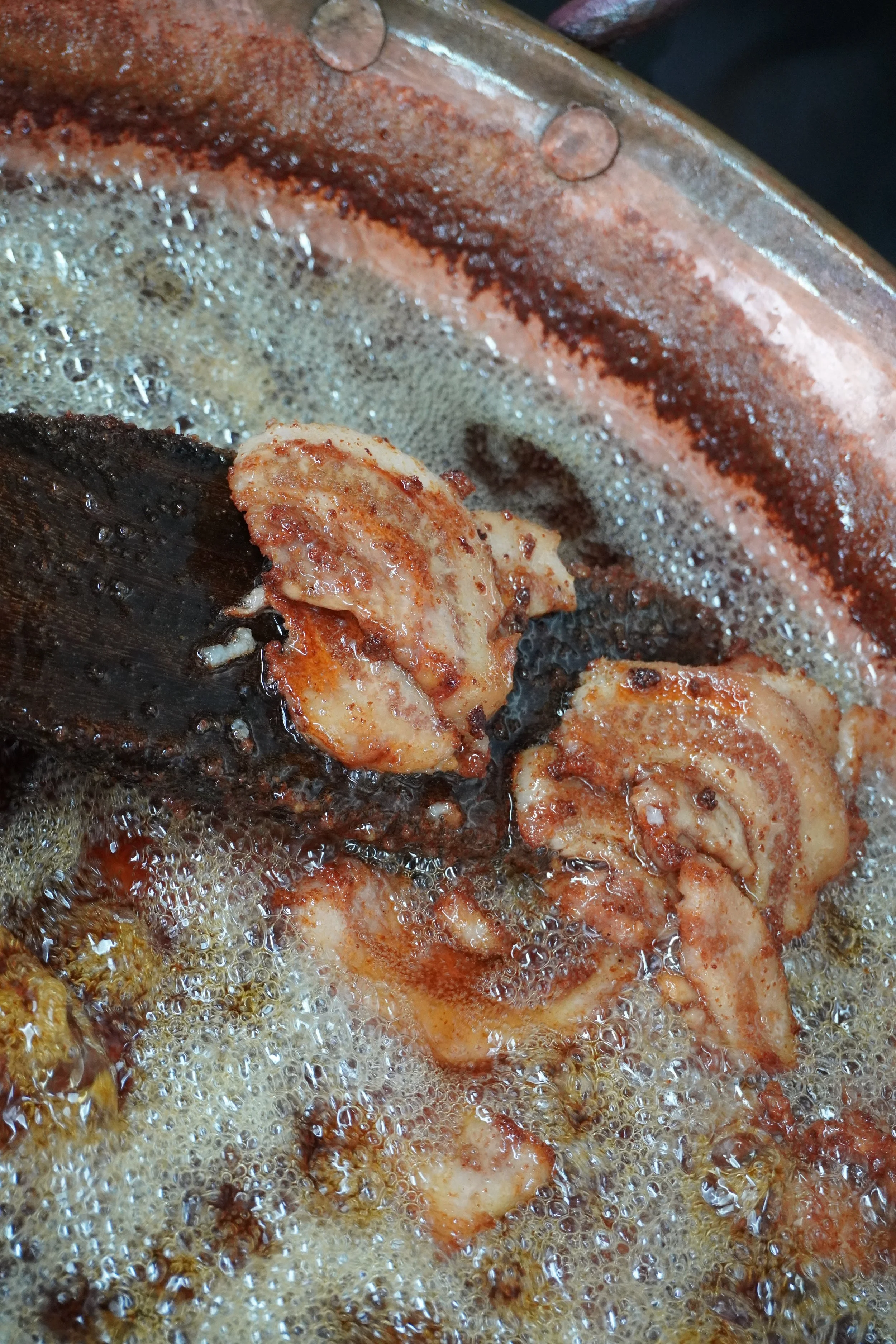 Frying pork pieces in hot oil in a cazo.