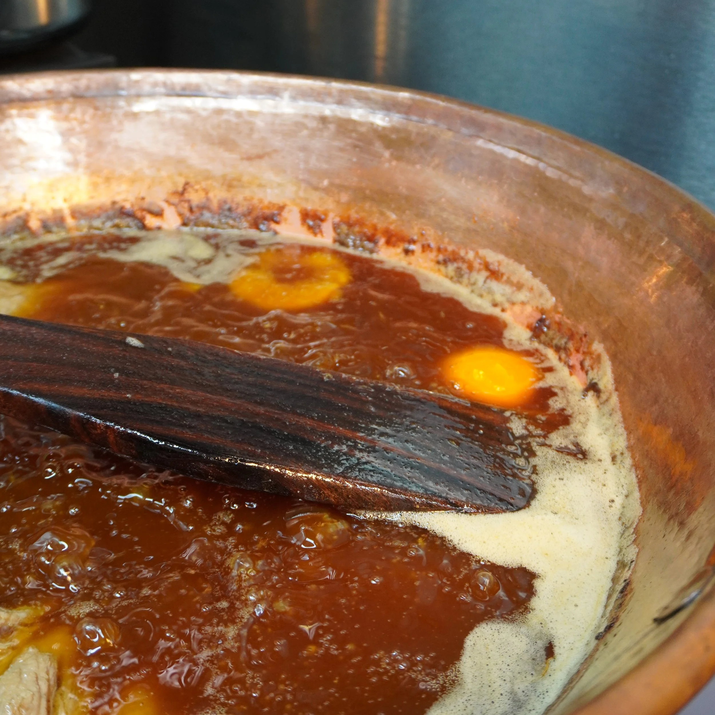 a copper cazo filled with brown liquid with a wooden shovel and a orange floating in liquid