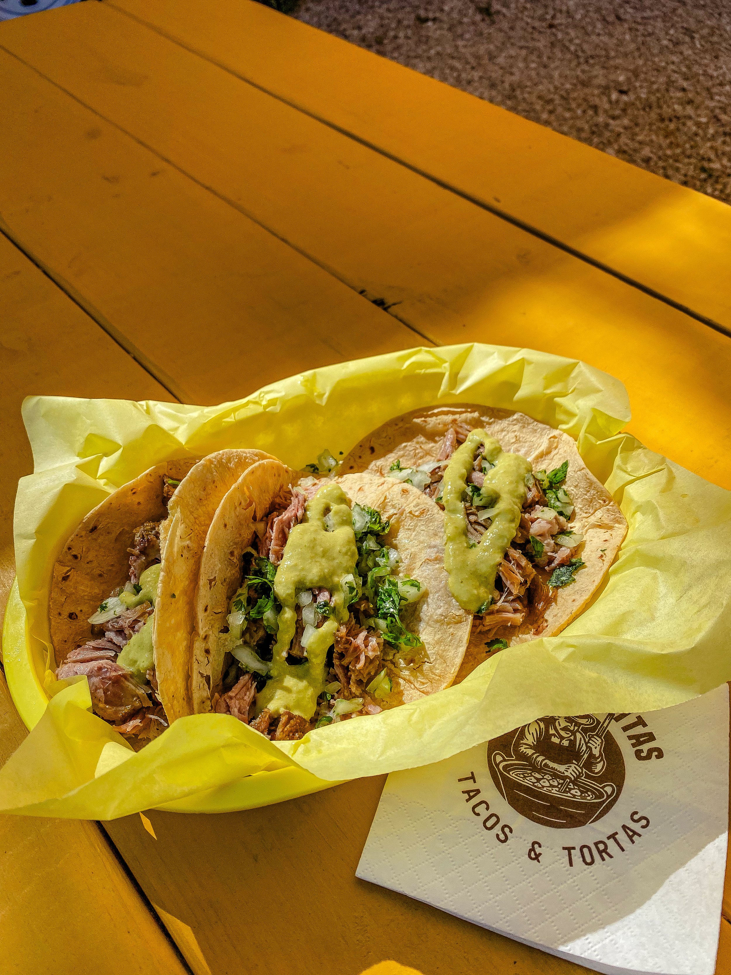 3 carnitas tacos on top a yellow picnic table with a napking