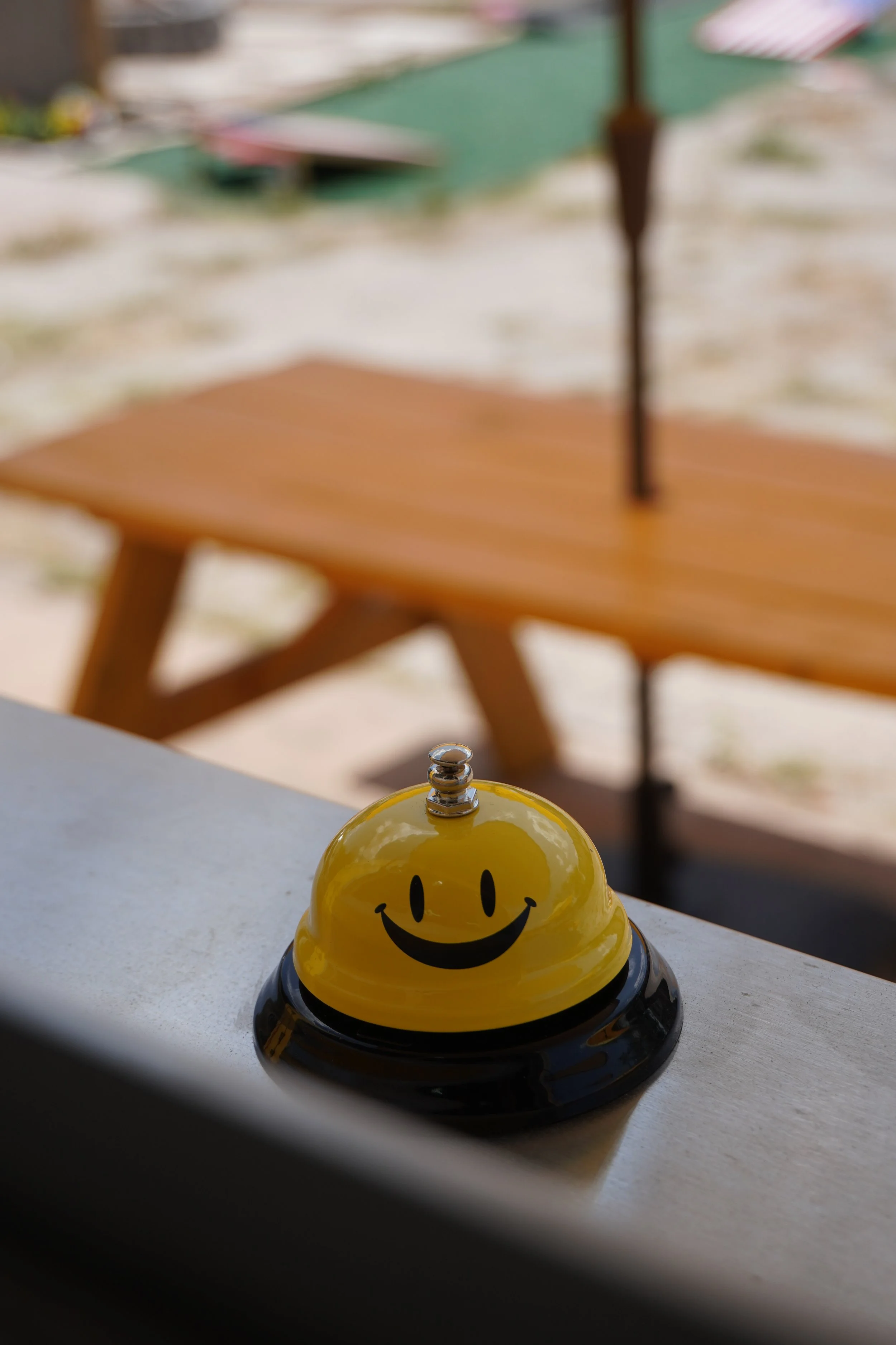 A small yellow smiley face timer with a black base on a white surface, with blurred outdoor patio furniture in the background.