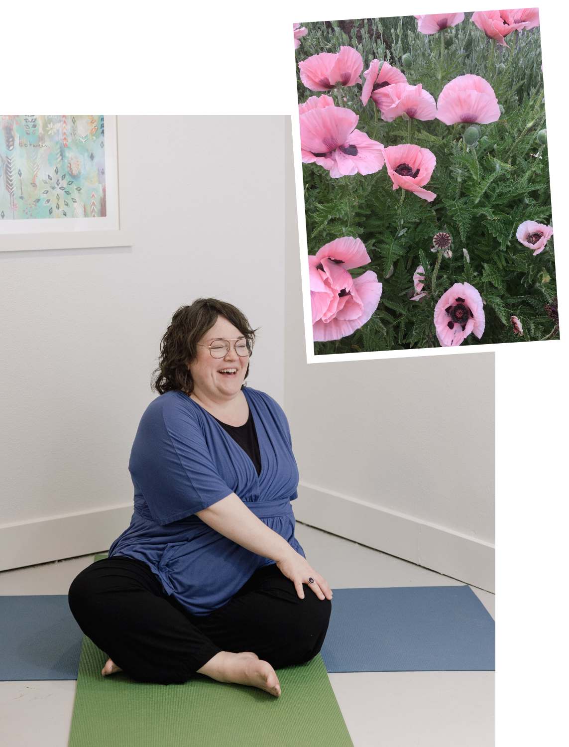 A woman with glasses, wearing a blue shirt and black pants, sits on a yoga mat laughing during a yoga or meditation session. There is a wall with artwork behind her, and a large print of pink poppies is projected or displayed in the space.