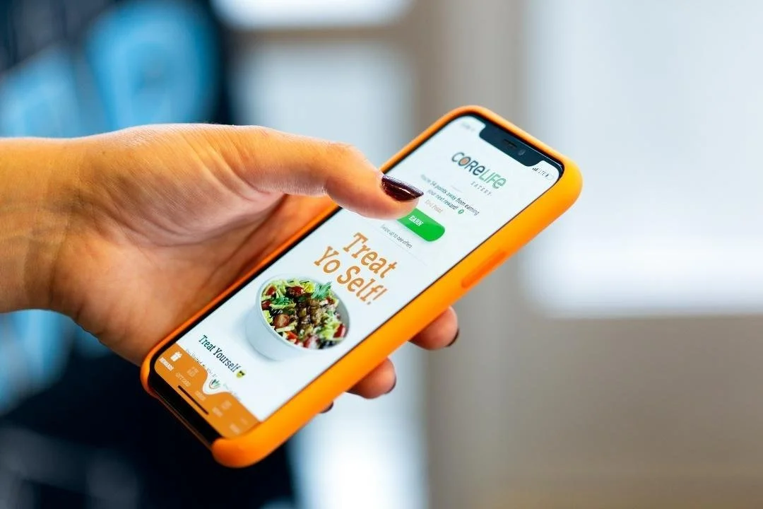 A person holding a smartphone with an orange case, displaying a health app called CoreLife with a focus on healthy eating and self-care.