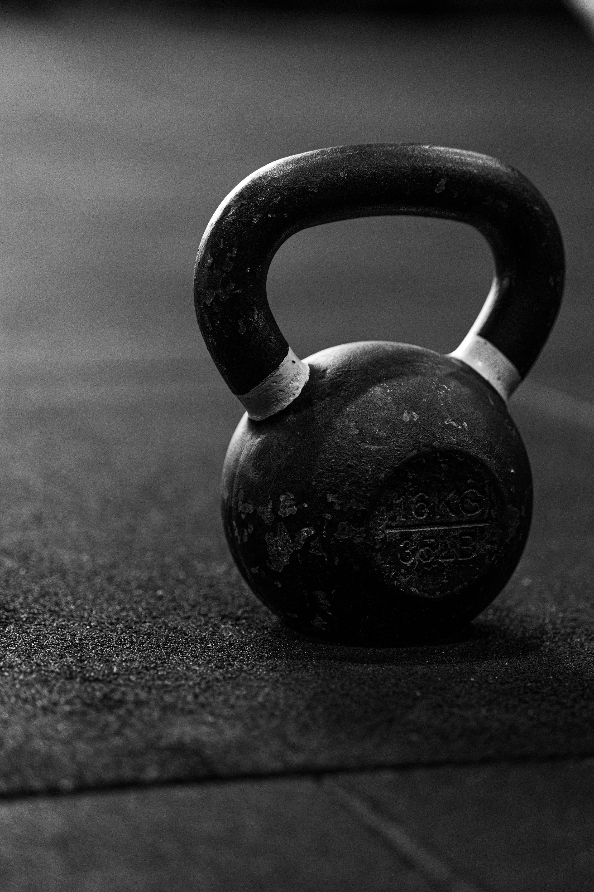 A black and white image of a kettlebell resting on a textured floor.