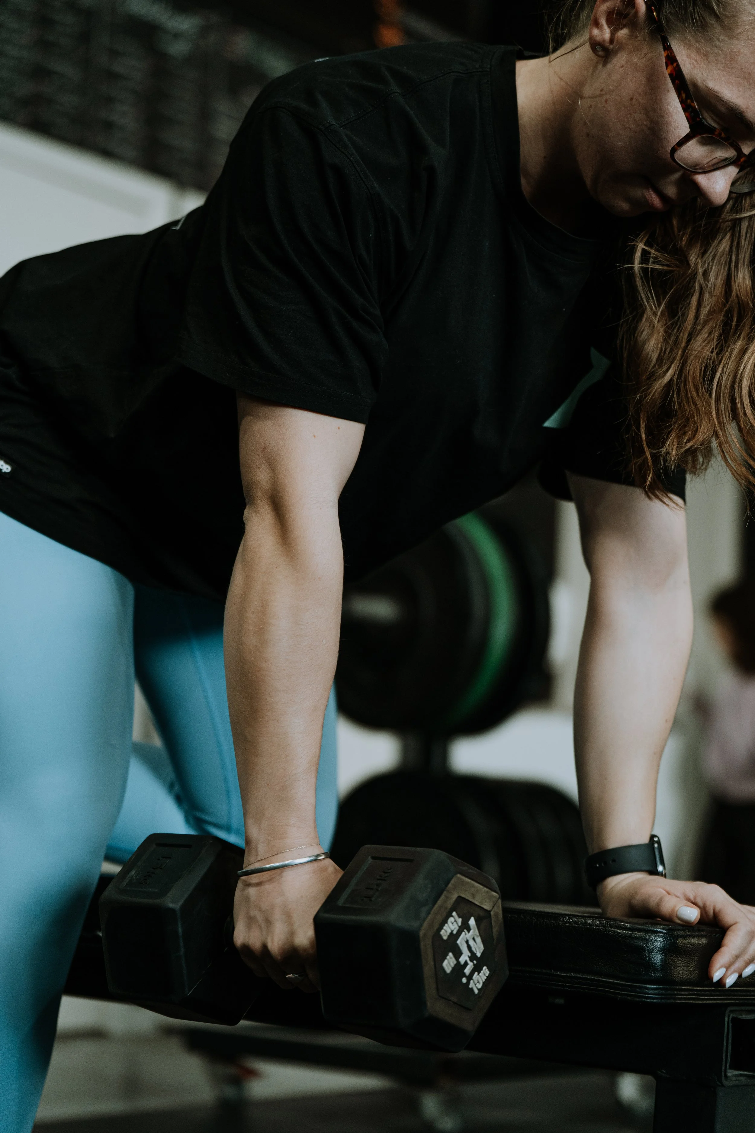 A woman performing a bent-over exercise with a dumbbell in a gym.