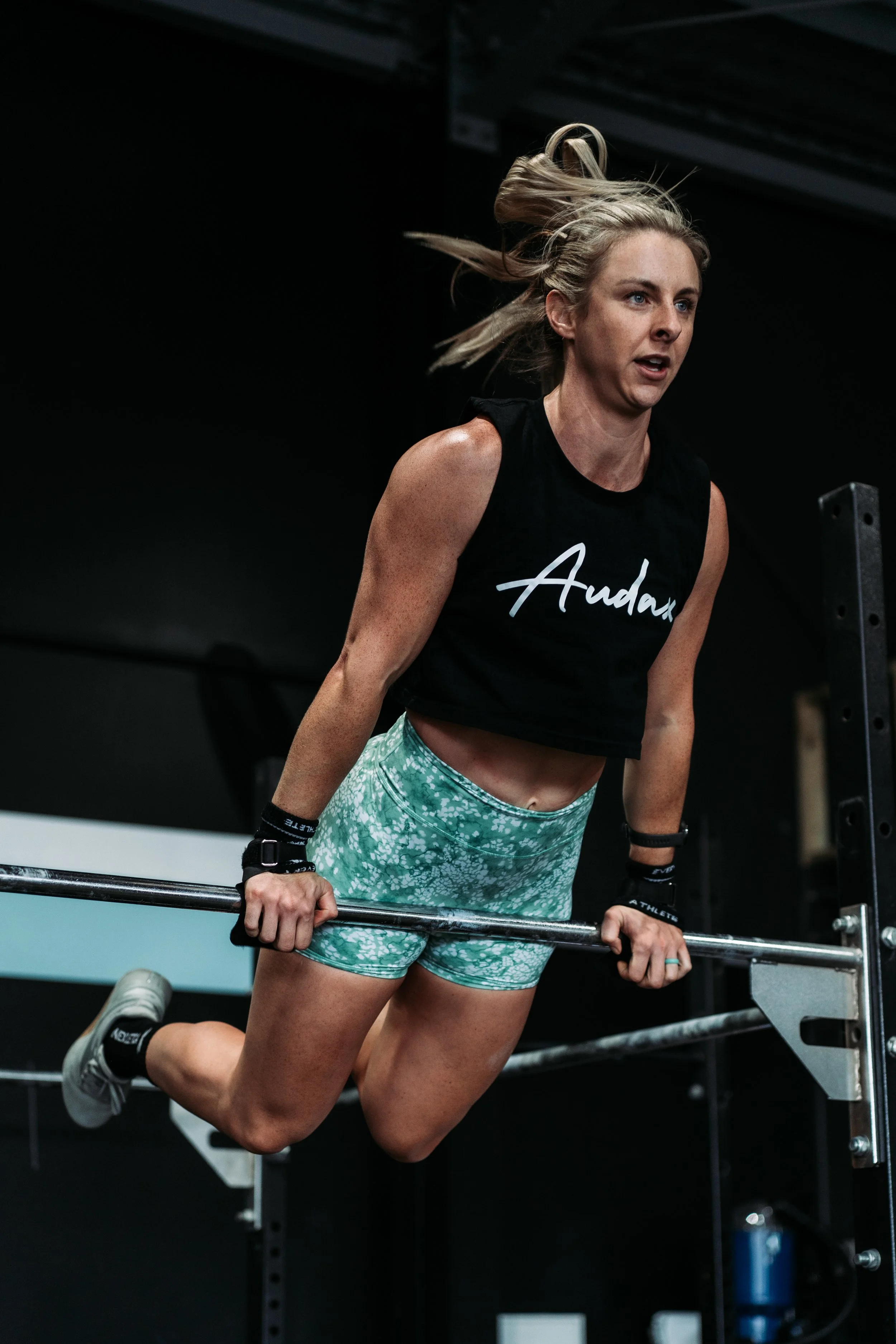 A woman performing a dip exercise on parallel bars in a gym, wearing athletic clothes.