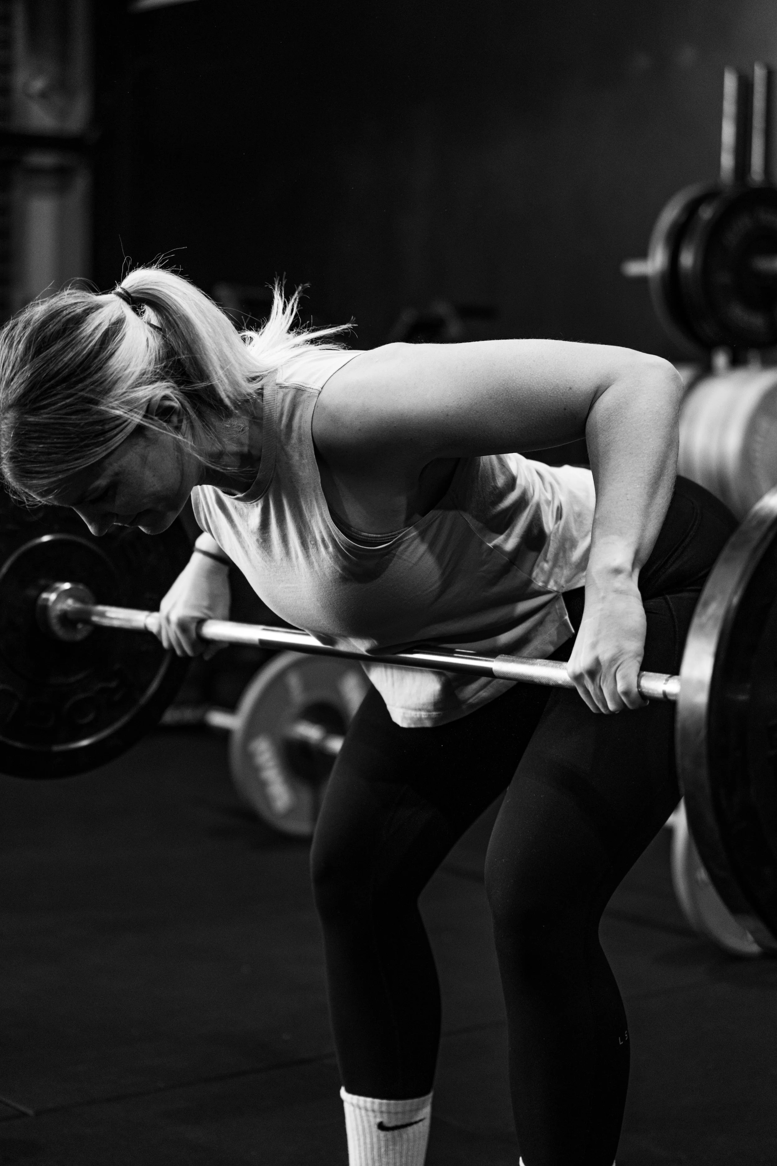 A woman lifting a barbell during weightlifting workout in a gym, black and white photo.