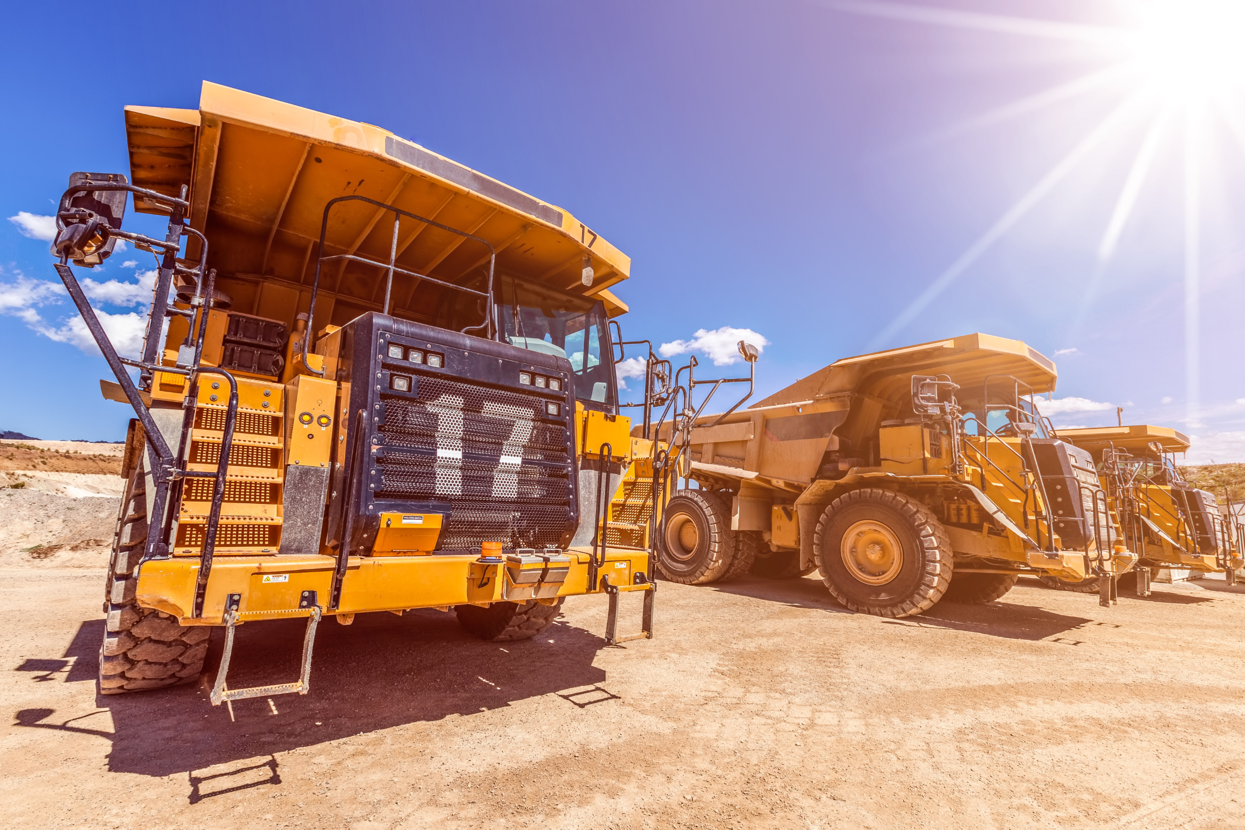 Row of large dump trucks on Mining site with sun flare