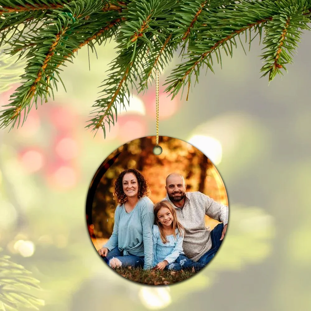 Christmas ornament with a family photo hanging from a pine tree branch.