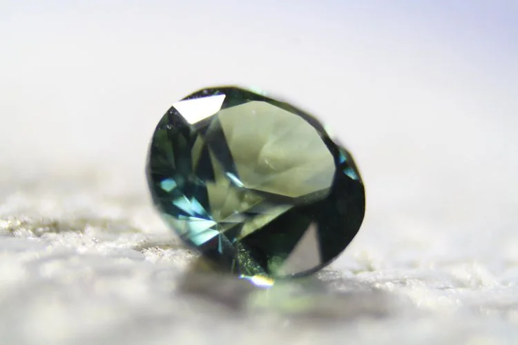 Close-up of a small, faceted gemstone on a soft surface.