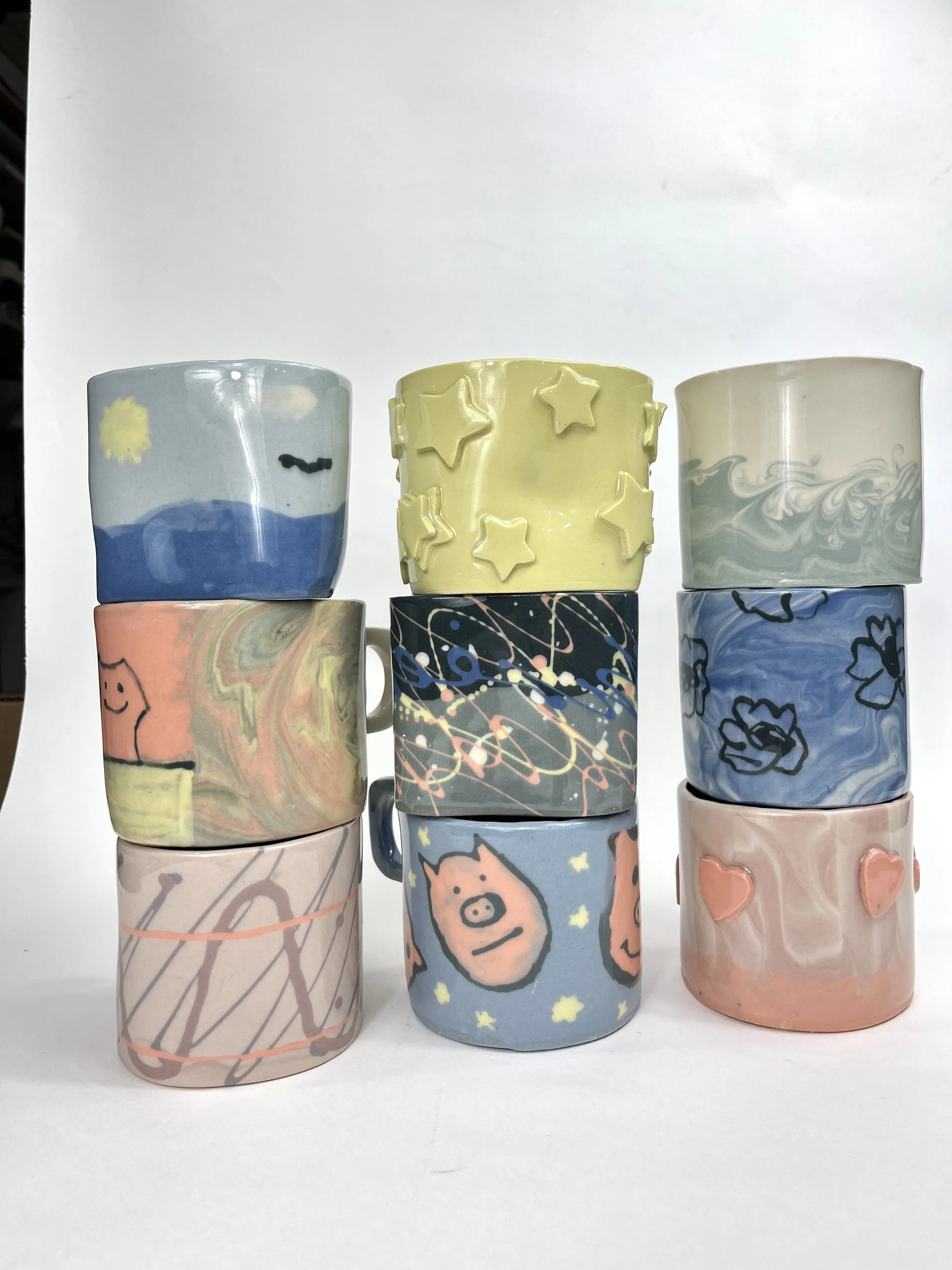 Ten decorated ceramic mugs arranged in three rows with colorful and artistic designs including pigs, stars, flowers, abstract patterns, and swirls.