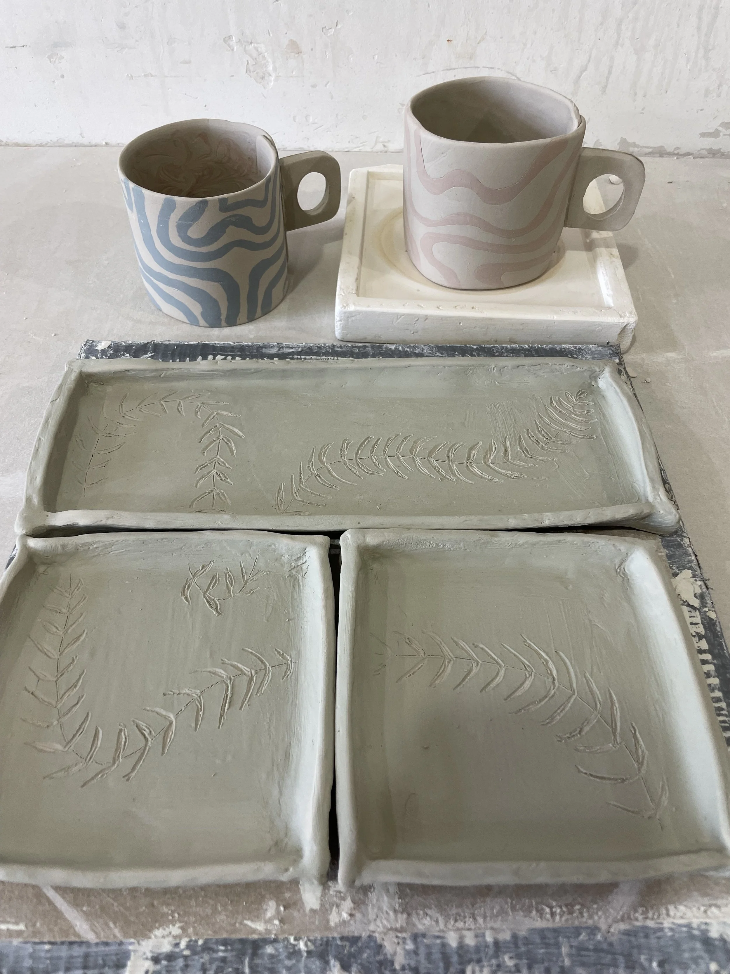 Handmade ceramic mugs and rectangular dishes with leaf patterns, placed on a table.