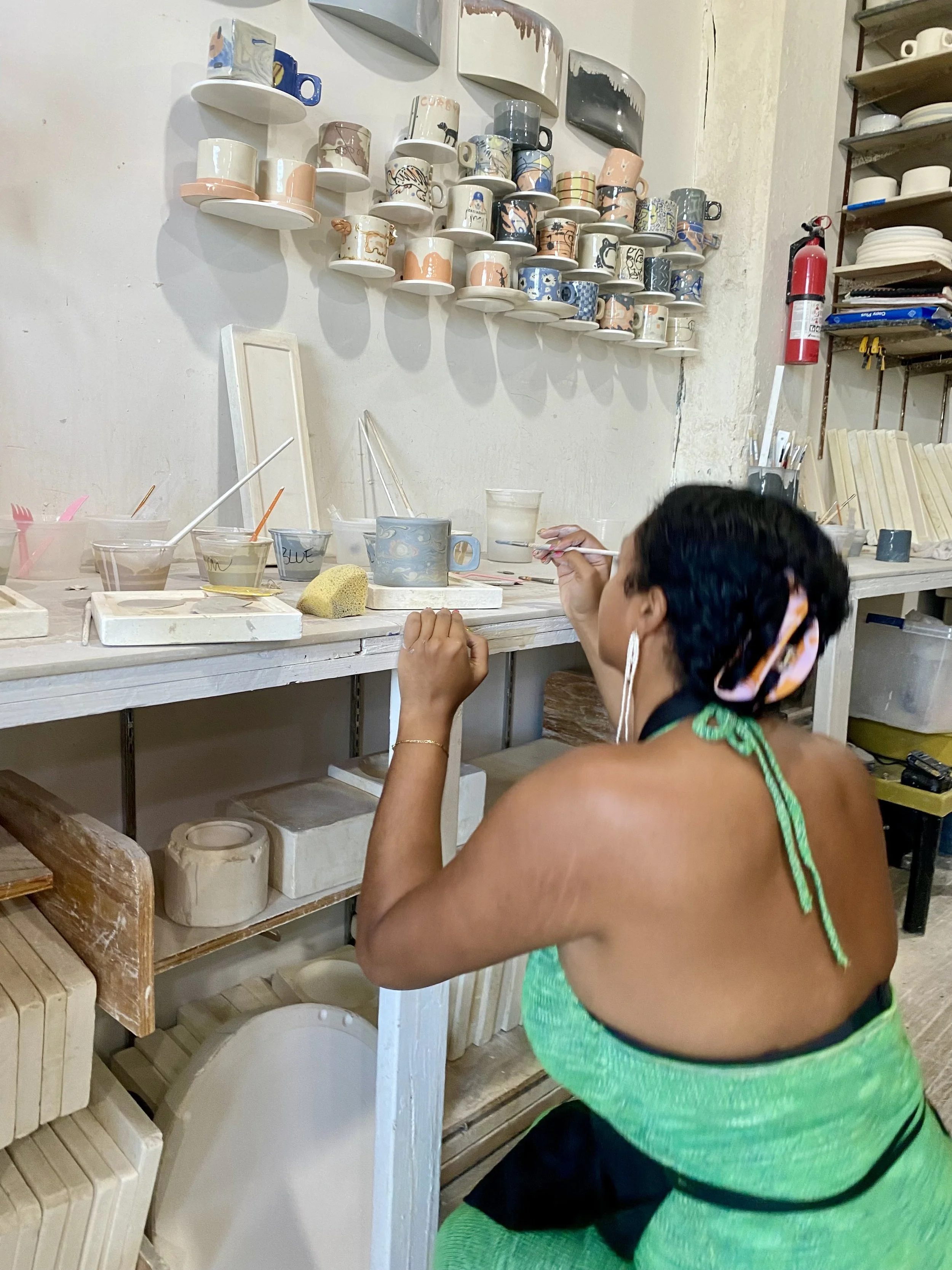 A woman painting and decorating handmade ceramic mugs created during a hand building workshop at our Brooklyn pottery studio.