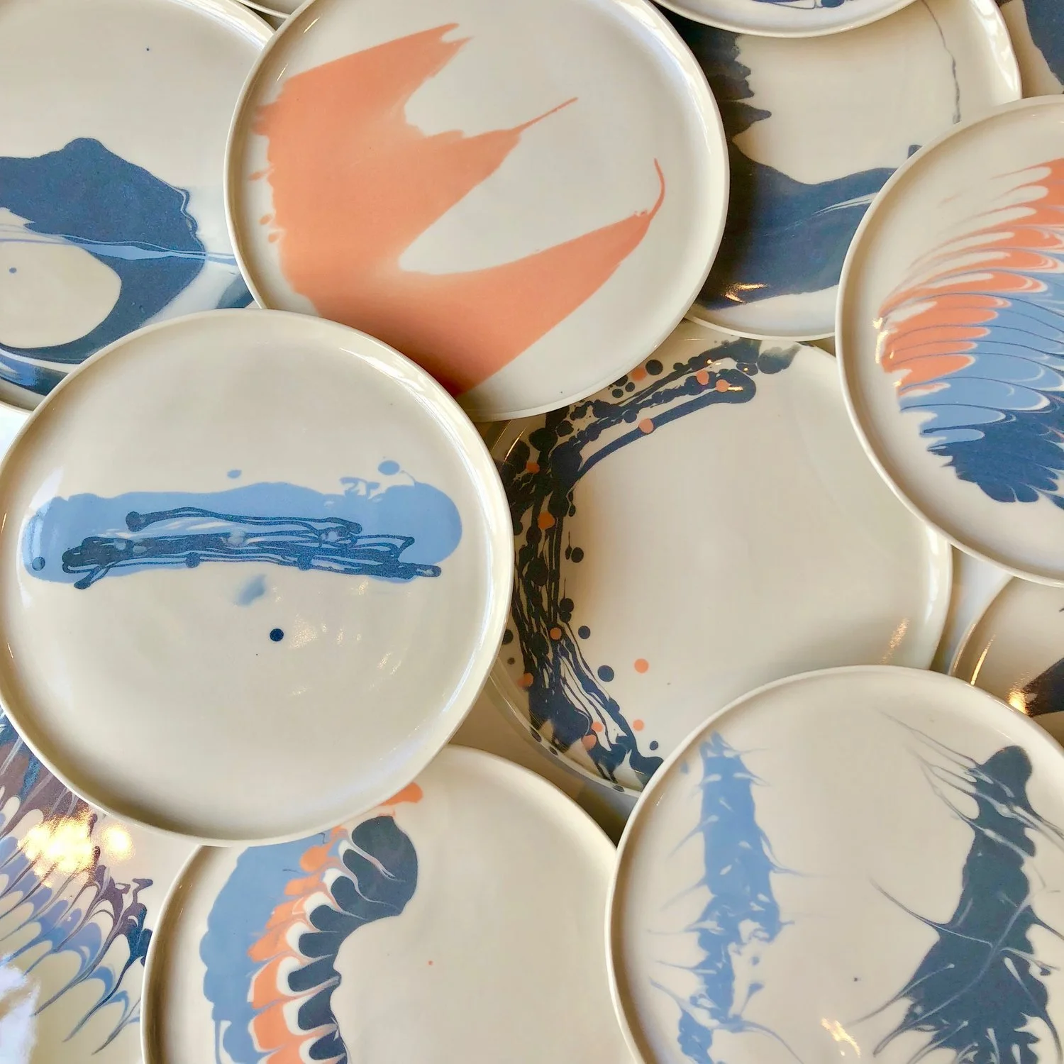 Multiple decorative plates with abstract blue and peach-colored designs layered on top of each other.
