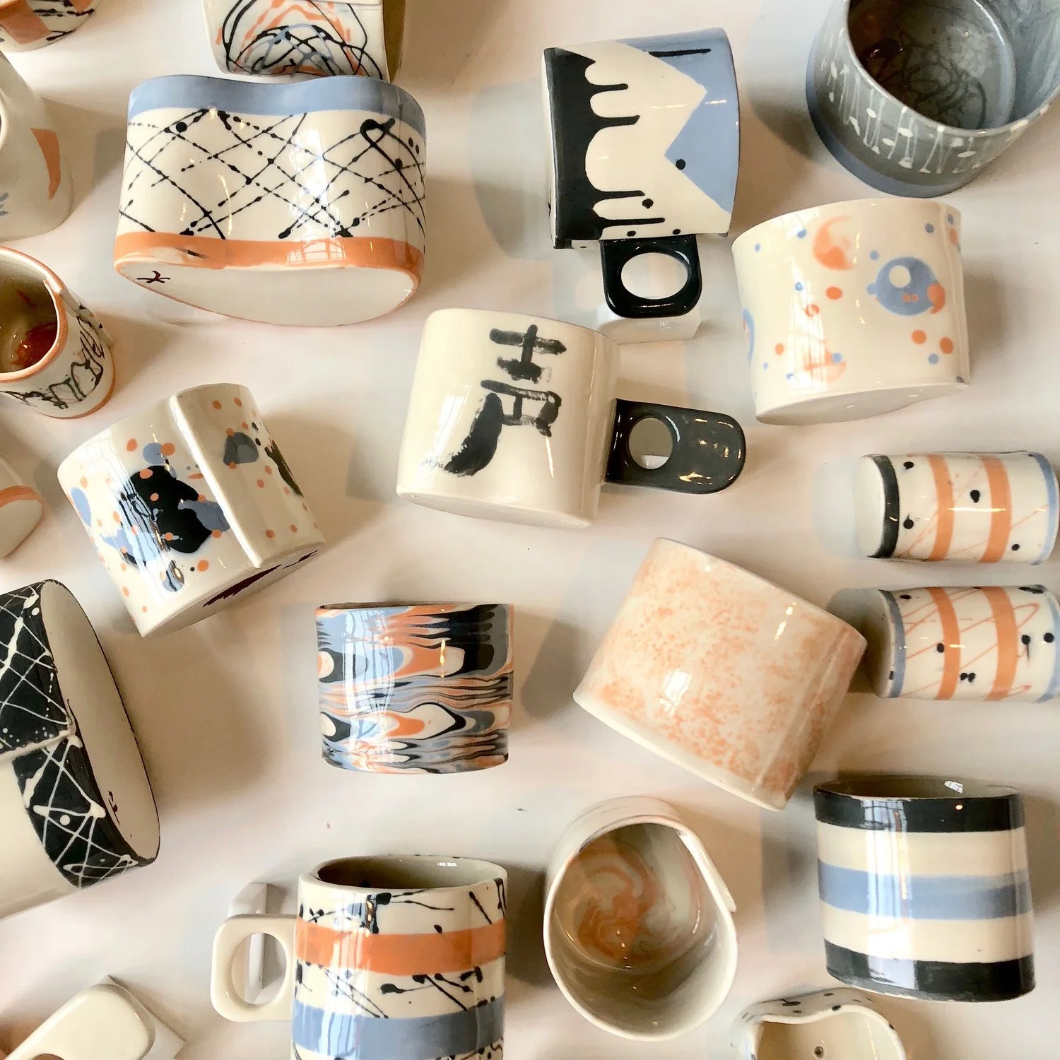 Various ceramic mugs and cups with abstract, geometric, and patterned designs, arranged on a white surface.