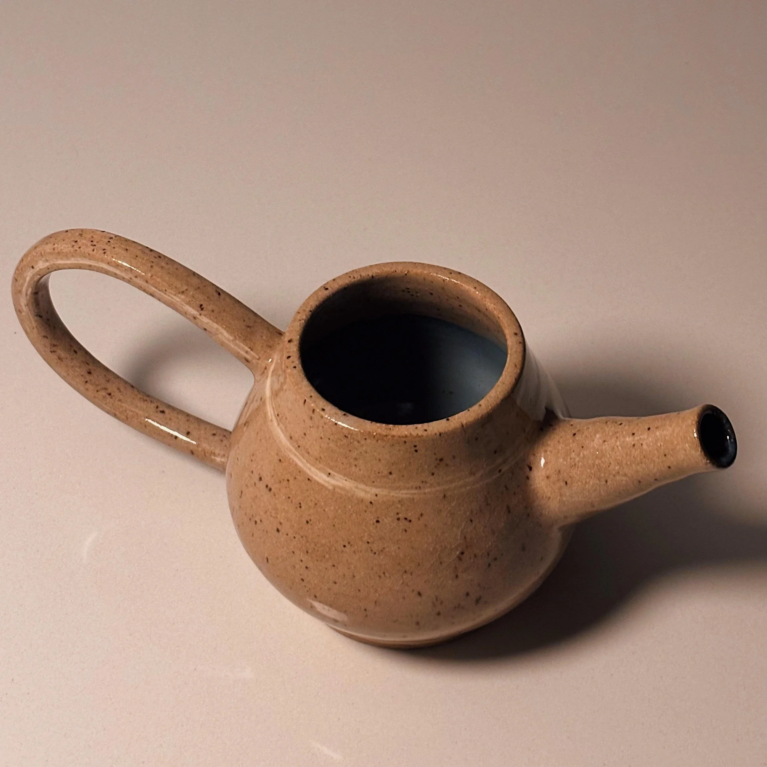 Small beige ceramic teapot with a curved handle and spout, sitting on a white surface.