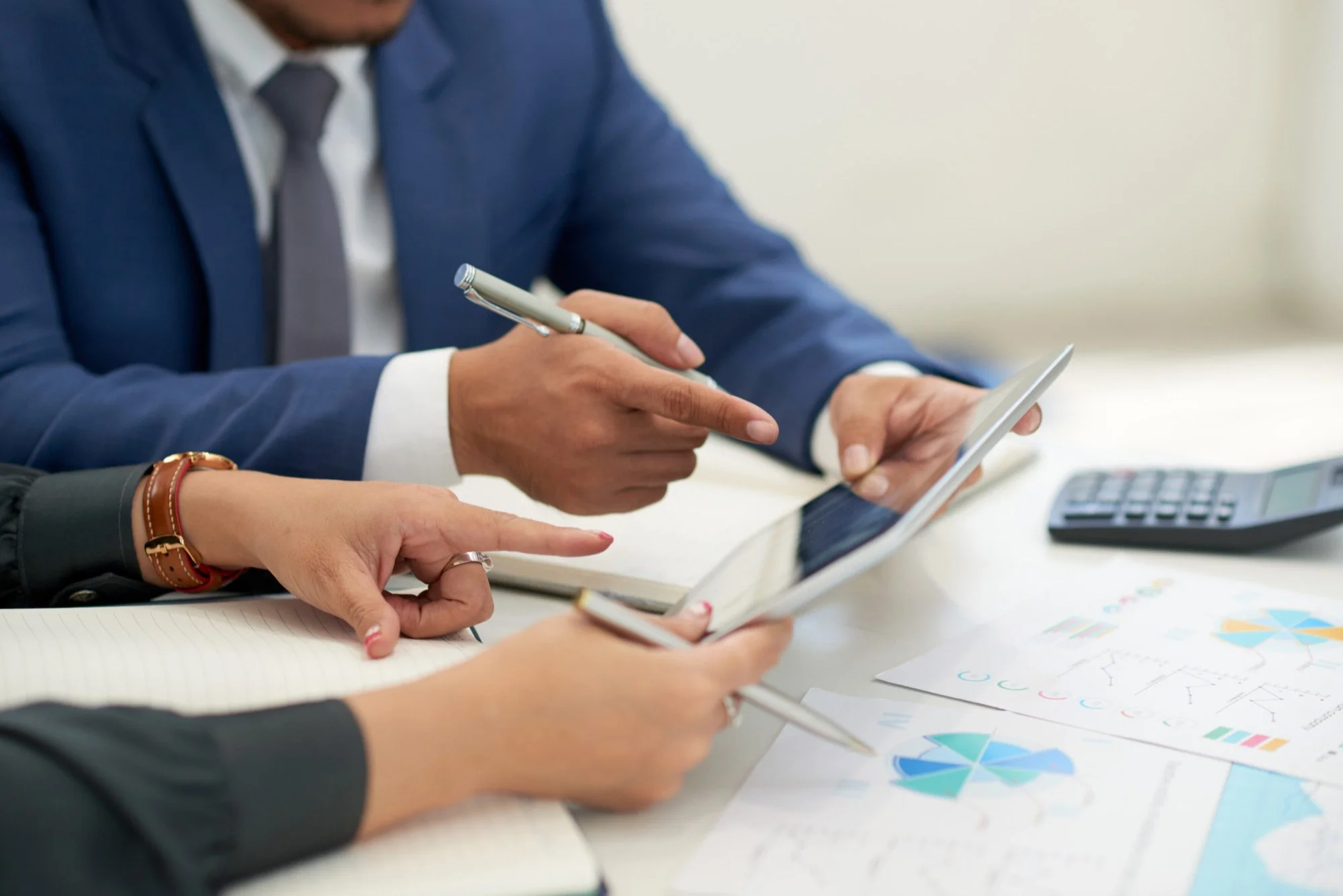 Two professionals in business attire reviewing financial charts and graphs, with a calculator, notebook, and documents on the table.