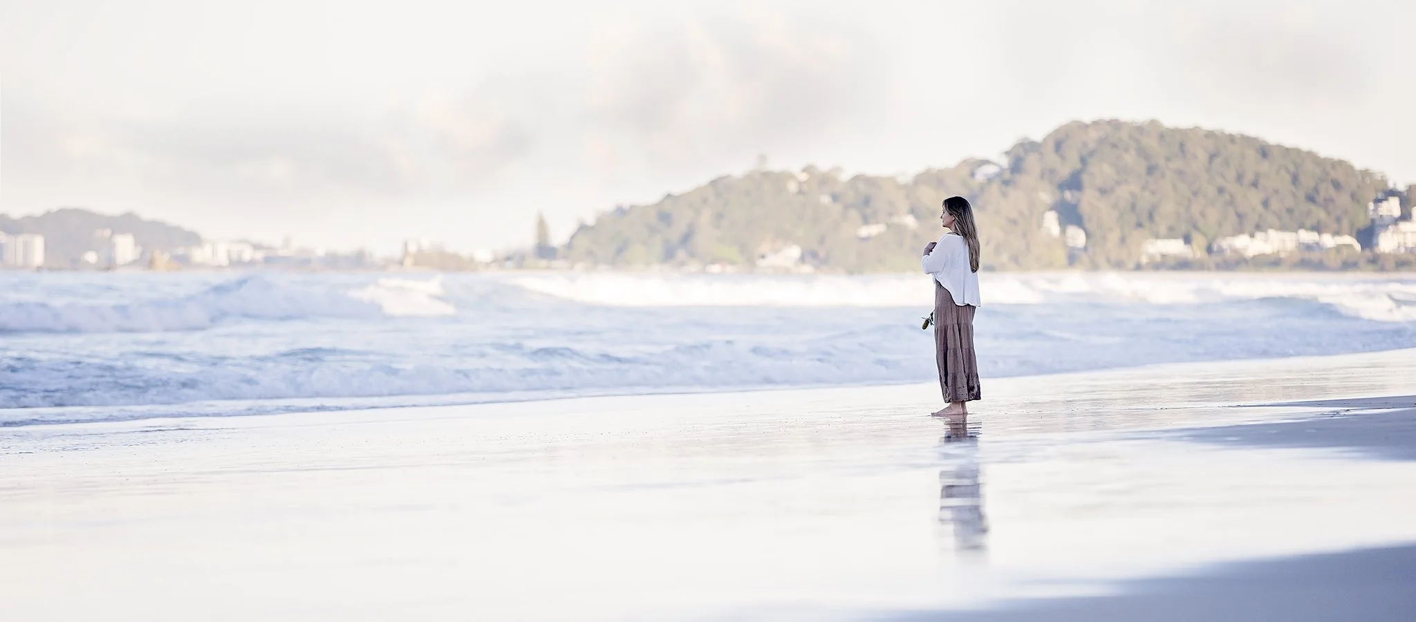 Woman on Gold Coast beach looking at the ocean during sunrise.
