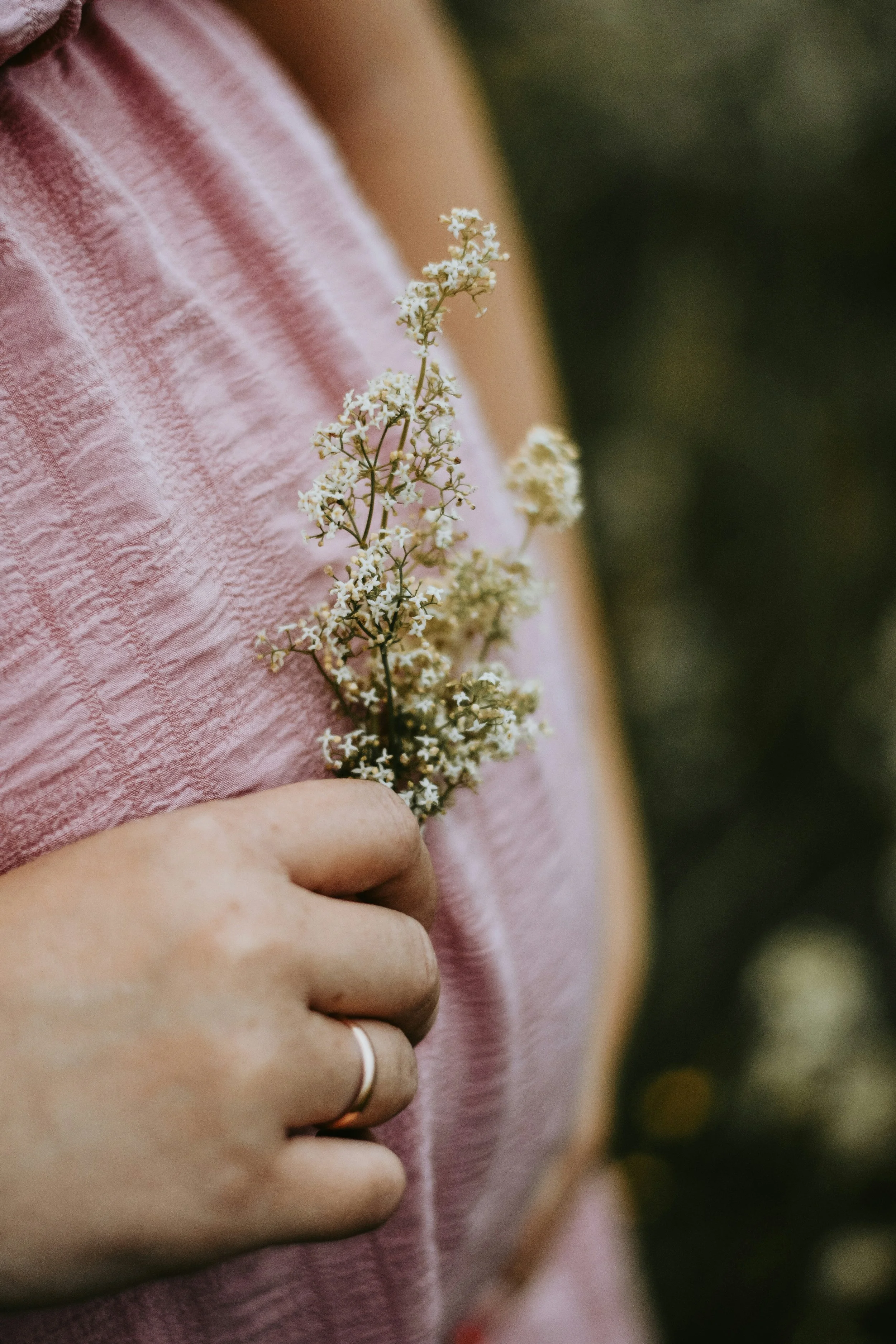 A person holding a small white flower against their pink textured dress.