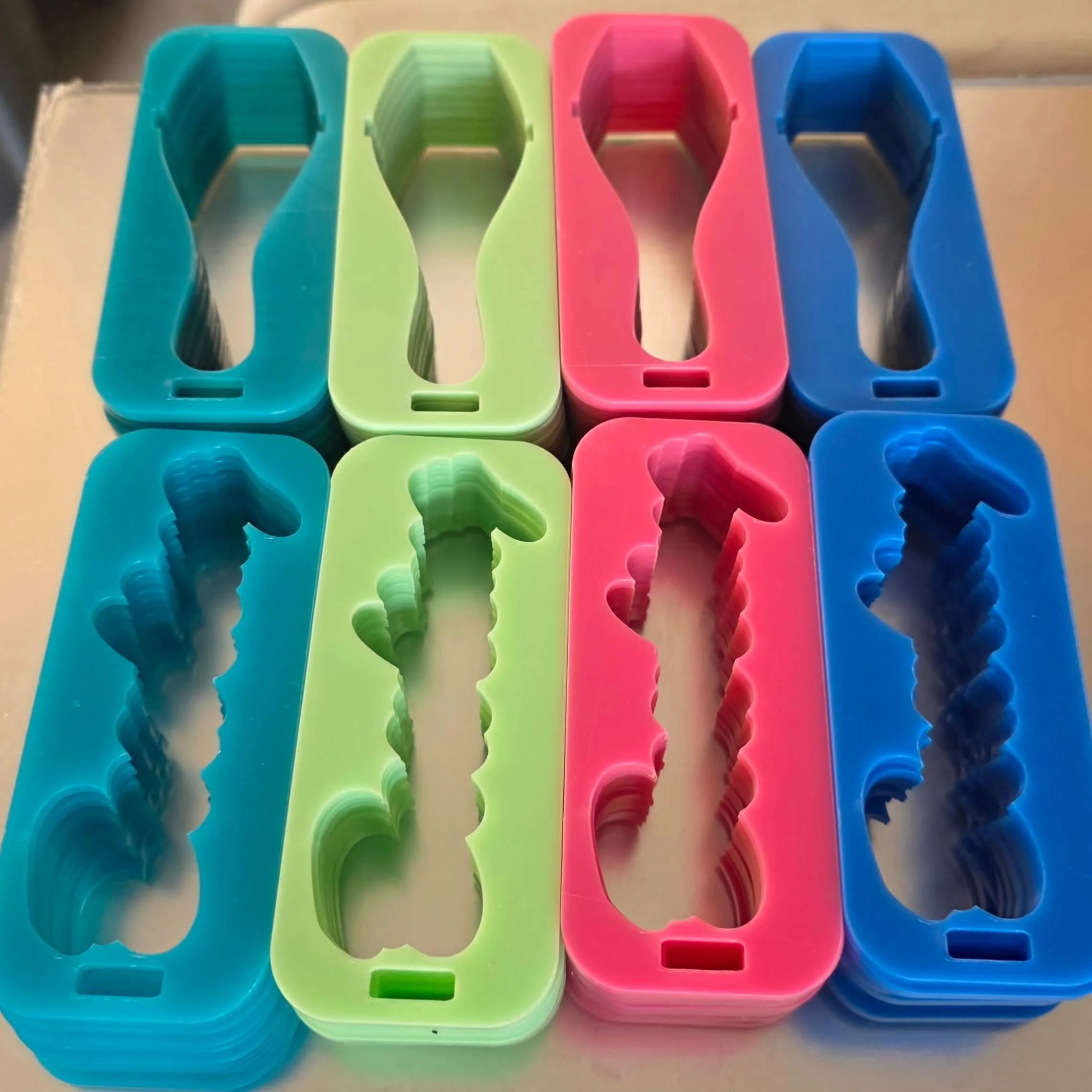 Colorful plastic cookie cutters in blue, green, pink, and dark blue, arranged in a row on a reflective surface.