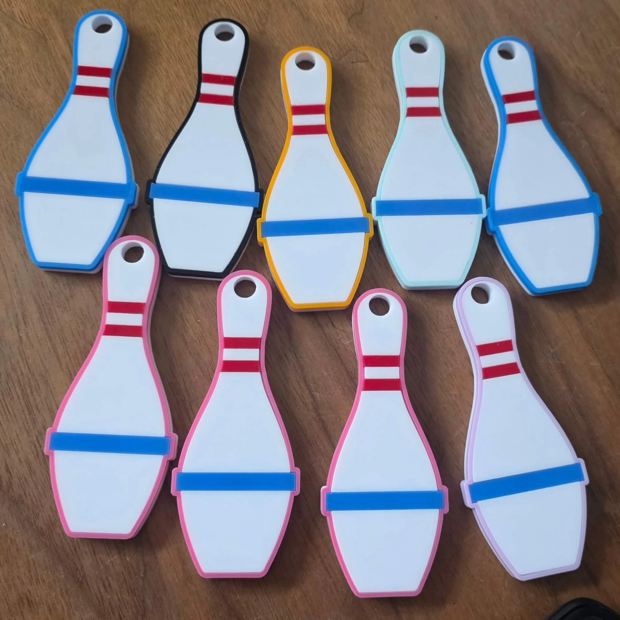 A row of five colorful plastic bowling pin-shaped markers with red stripes, each with a small hole at the top, placed on a wooden surface.