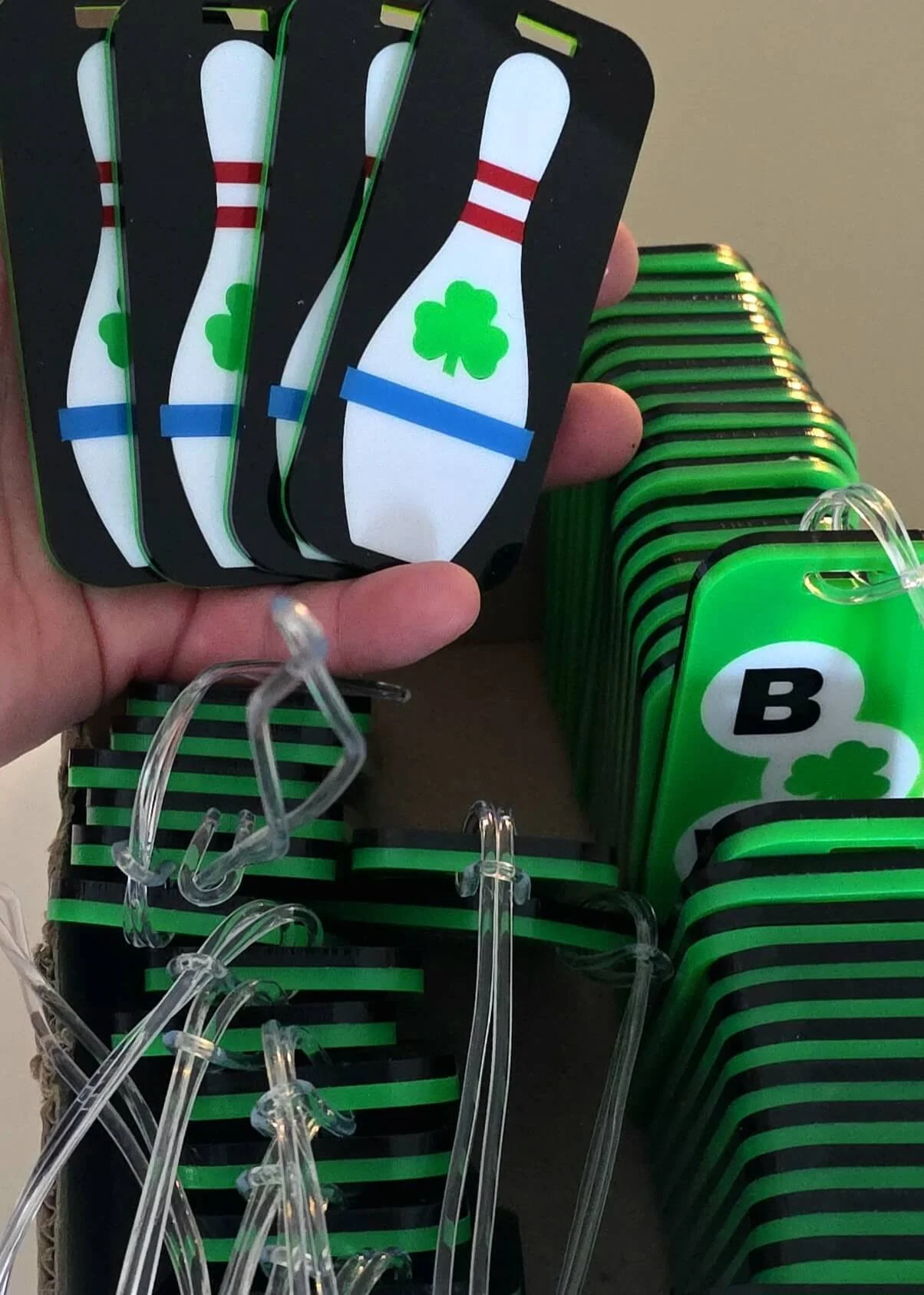 A hand holding four cards with bowling pin and shamrock designs. Behind, there are green and black cards and clear plastic hooks on display.