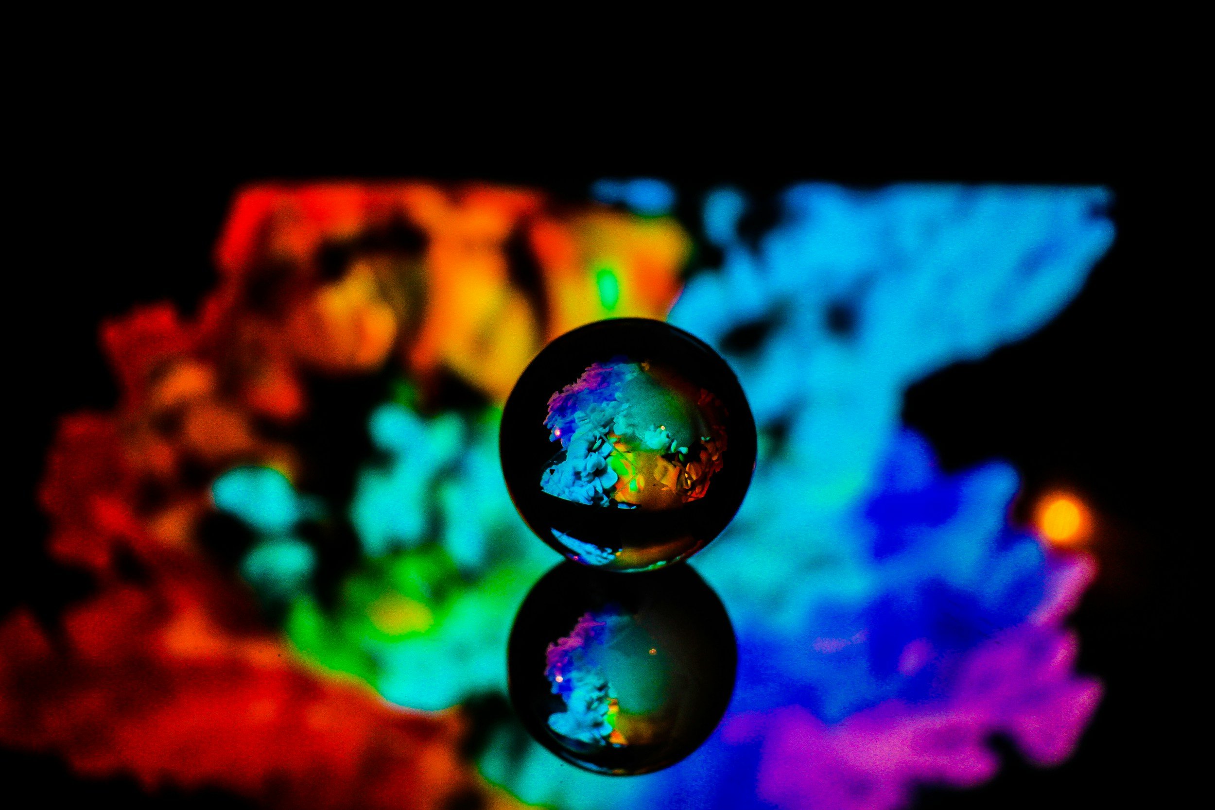 Close-up of a glass sphere reflecting colorful abstract lights against a dark background.