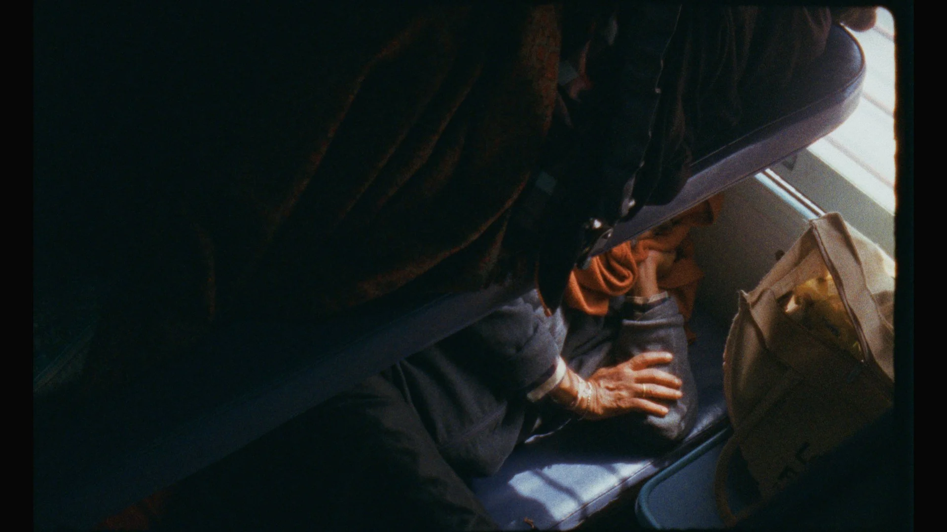 A person sleeping on a bus seat with a bag beside them, seen from above.