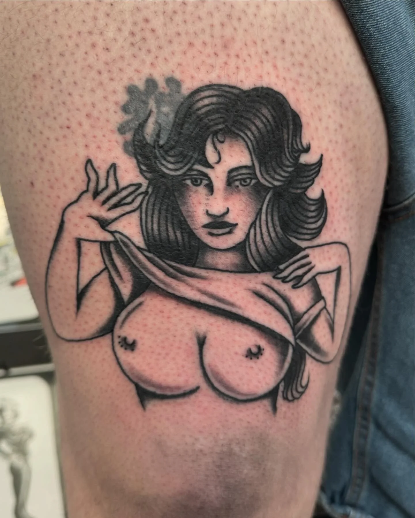 Tattoo of a woman with flowing hair and a flower in her hair, lifting a shirt to reveal cleavage, with red shading in the background.