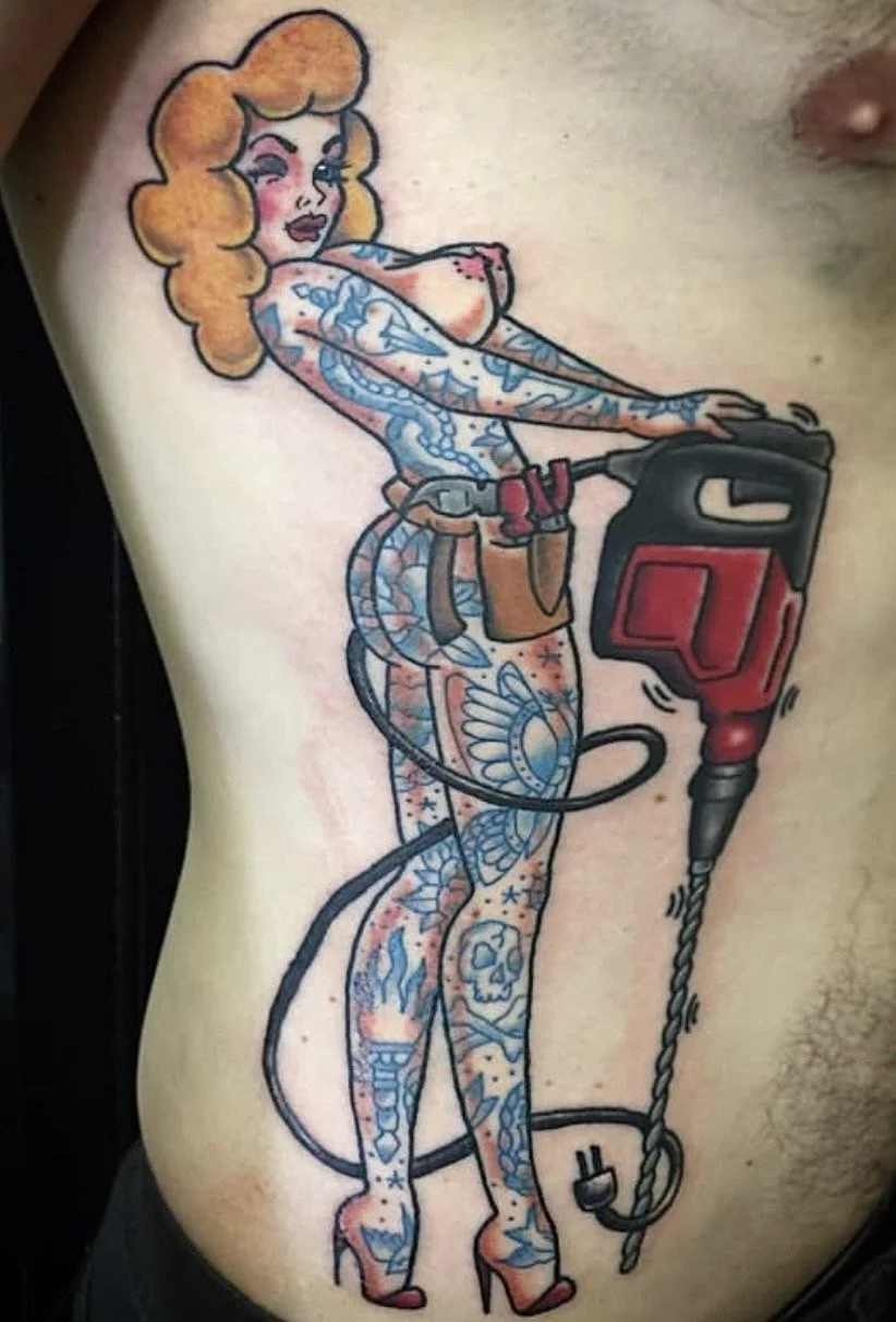 Tattoo of a cartoon woman with orange hair, tattoos covering her body, holding a power drill with a provocative pose.