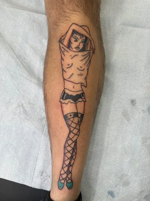 Tattoo of a woman with a hat, topless, wearing shorts and fishnet stockings on a person's leg.