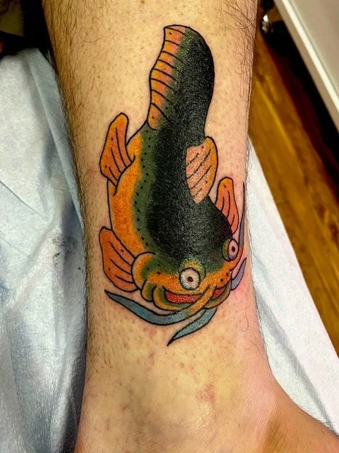 Colorful fish tattoo with prominent eyes and fins on a person's leg.
