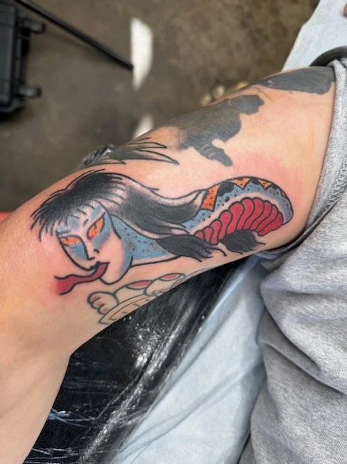 Tattoo of a snake with a fierce face and an open mouth, wrapping around a person's arm.