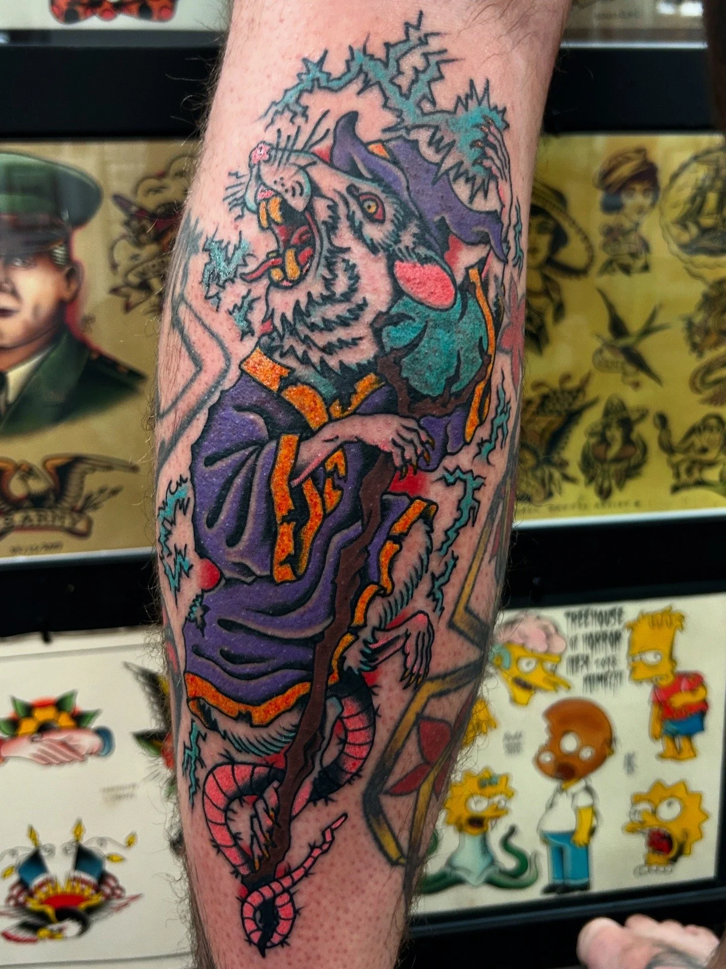 Tattoo of a rat with lightning, a tree branch, and a serpent, with bold black outlines and vibrant colors on a person's leg. Best color tattoos in northern Colorado. Amazing tattoo work