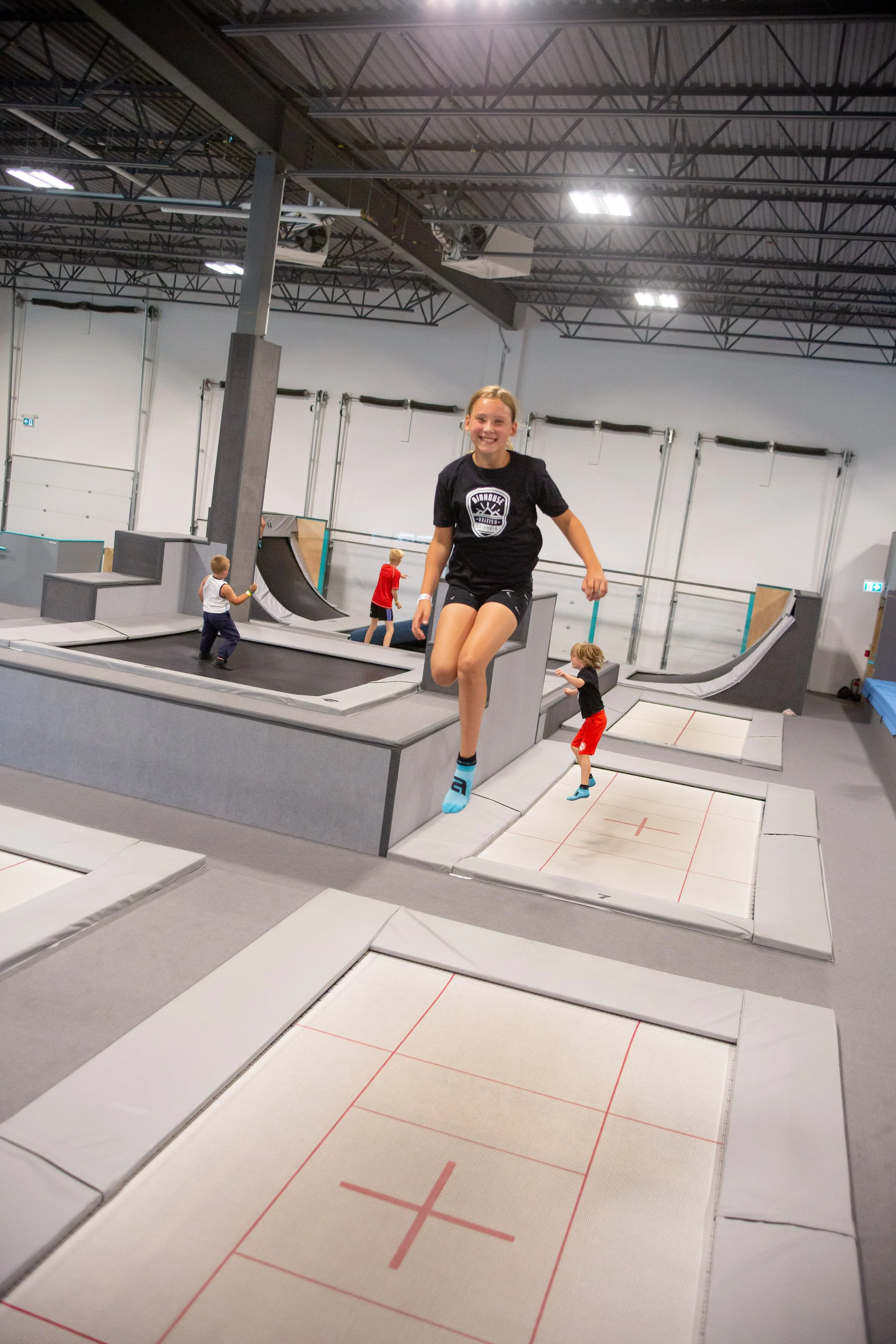 Children playing on indoor trampoline park with foam pits and various jumping surfaces.